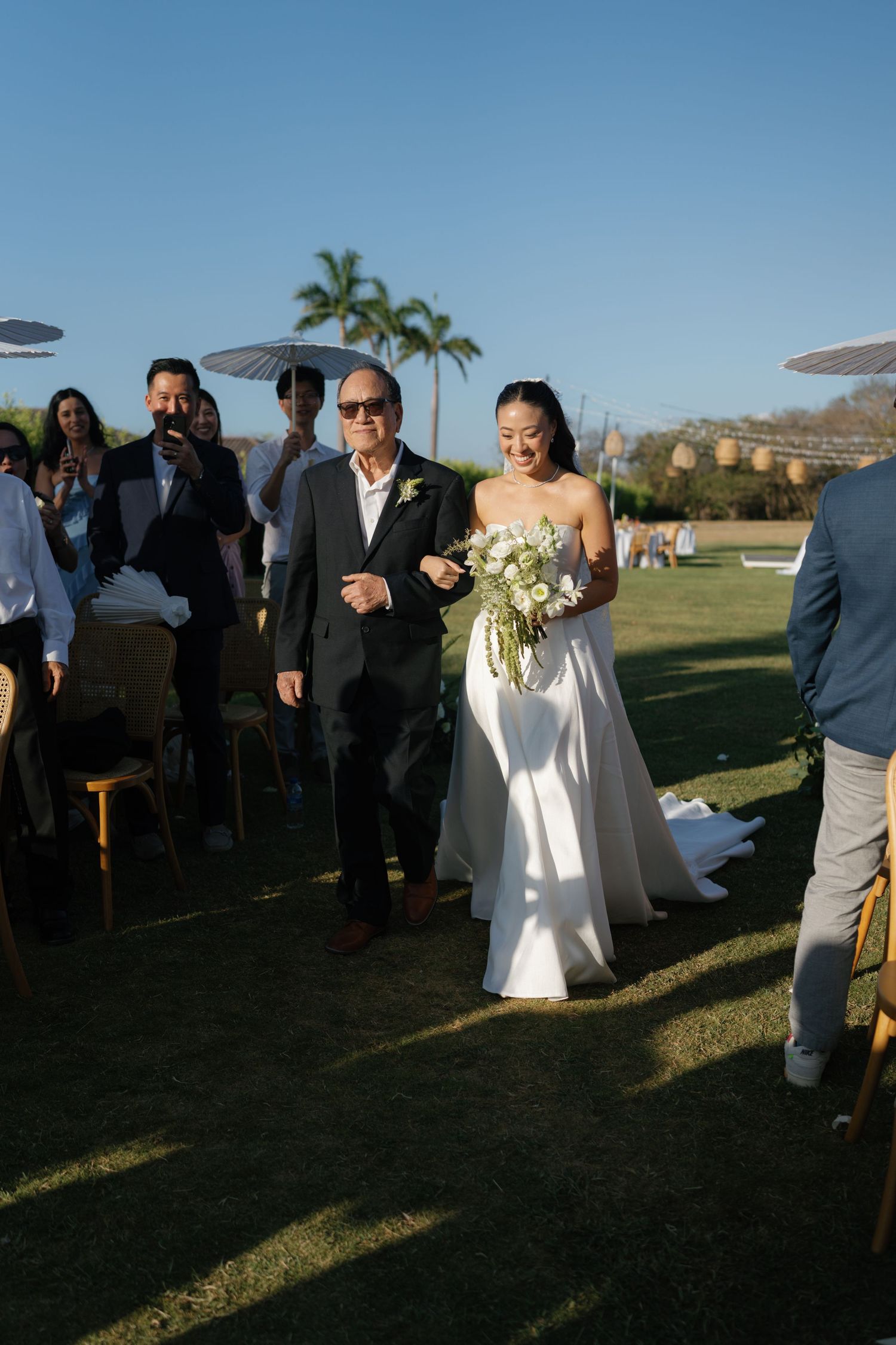 Outdoor wedding ceremony on a grassy lawn with ocean views and white parasol decorations.