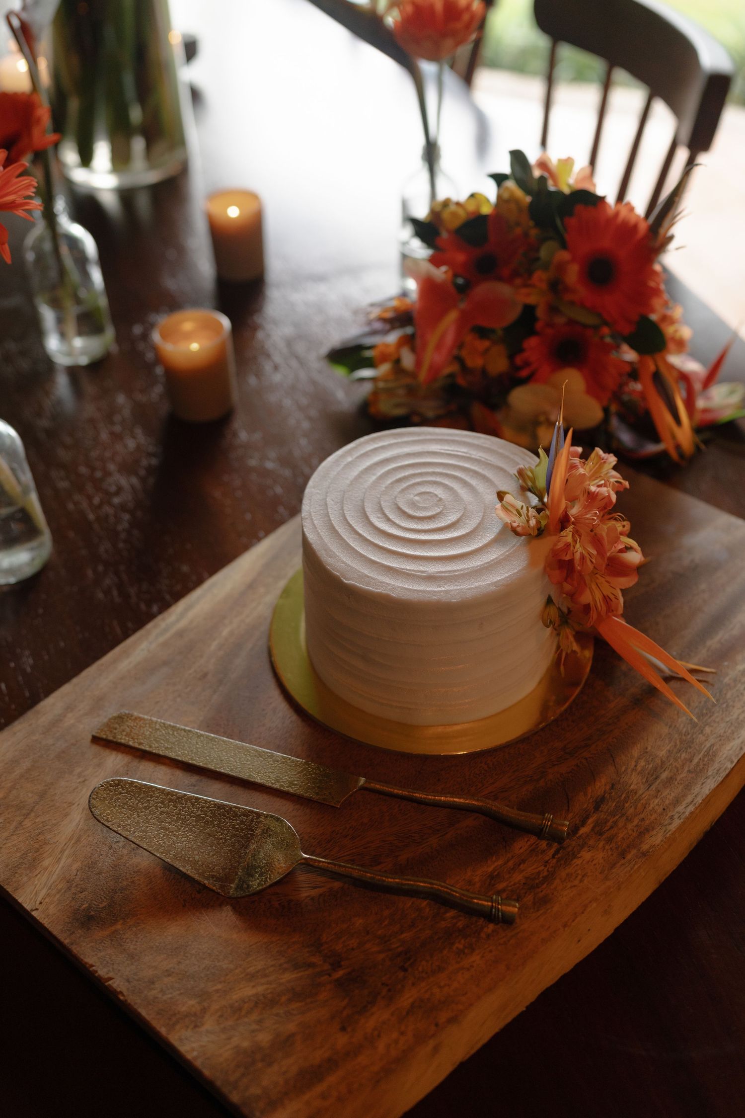 White frosted wedding cake decorated with orange flowers on a rustic wooden board.