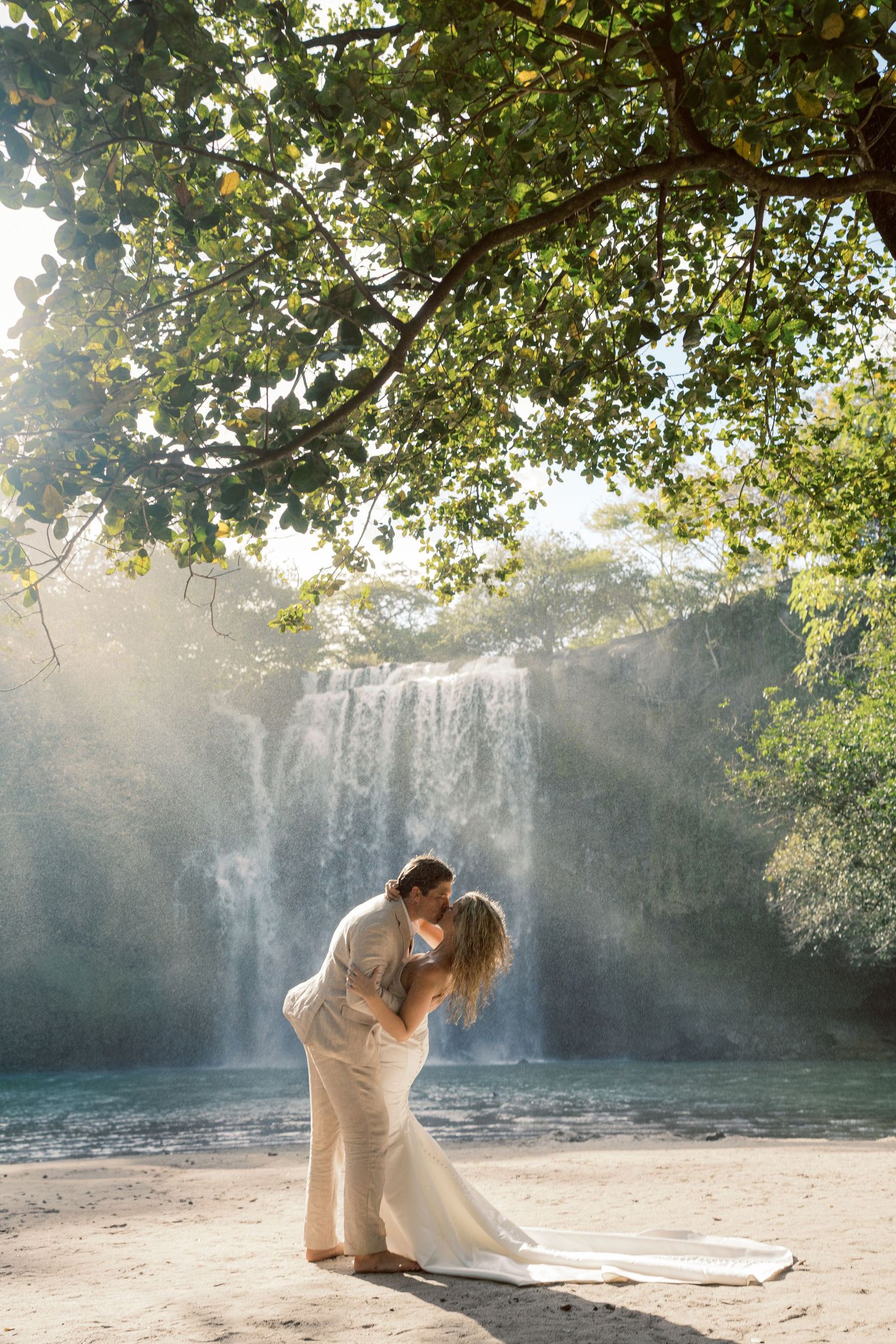 Dancing figures in light-colored clothing move elegantly against the backdrop of a misty waterfall.