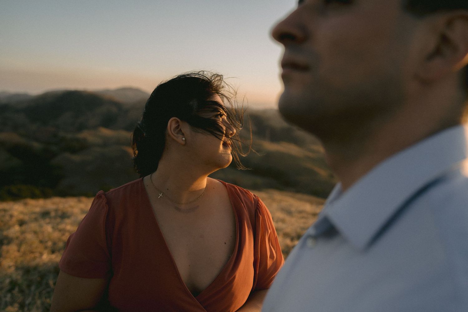 A couple shares an intimate moment in warm sunset lighting on a hilltop.