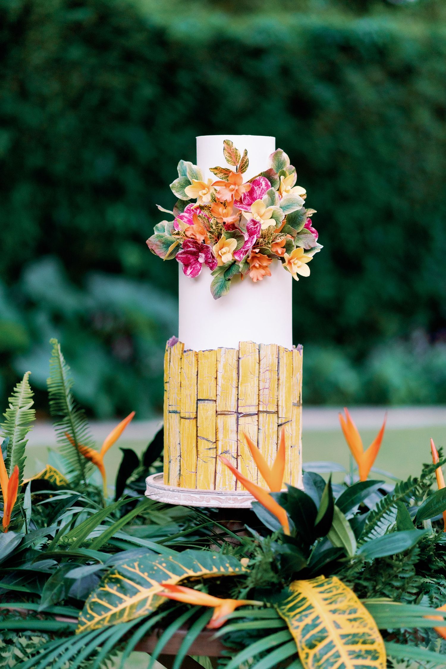 White and gold tiered wedding cake decorated with pink flowers and tropical foliage.