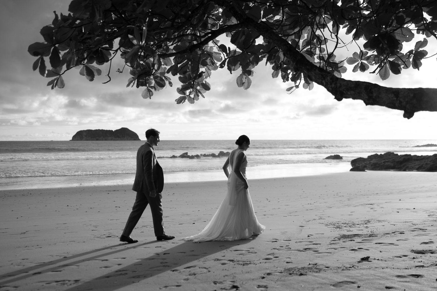 A series of black and white beach wedding photos showing couples walking along the shoreline at sunset.