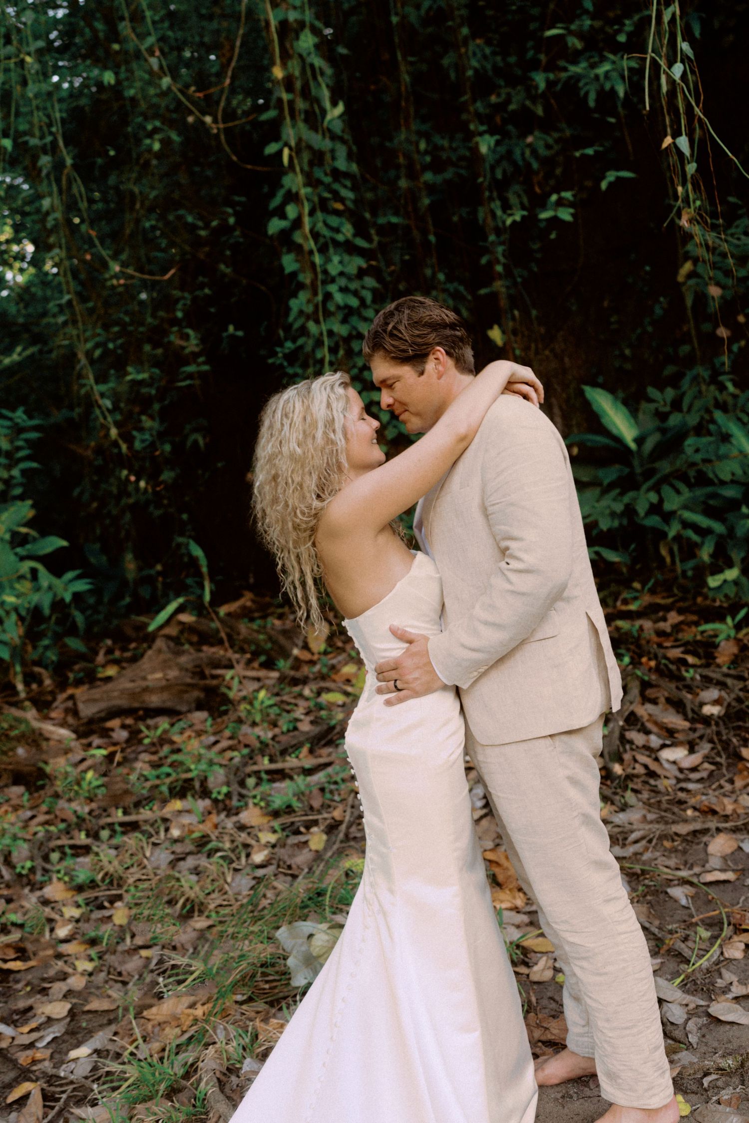 A romantic moment unfolds between a couple in white attire surrounded by lush greenery.