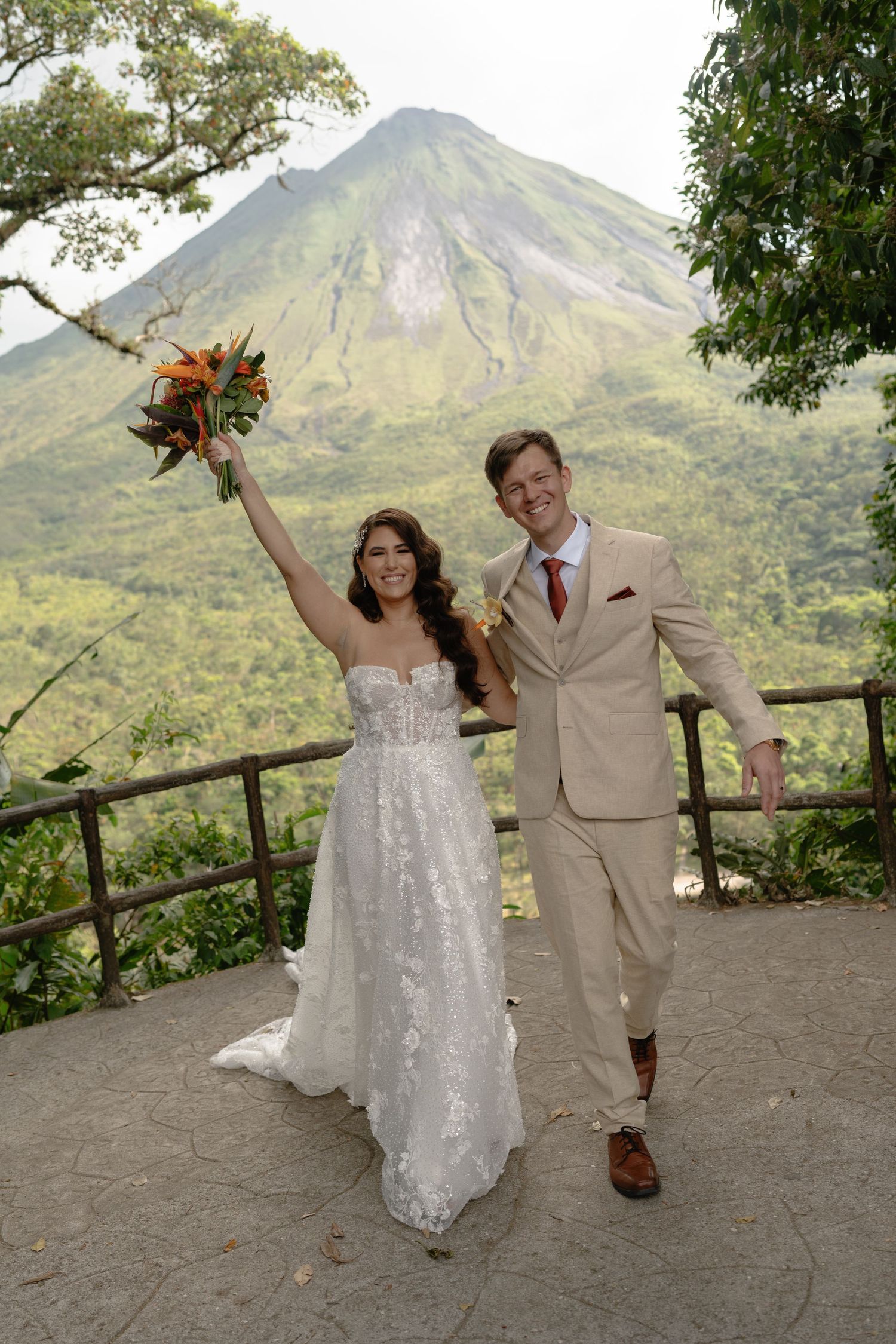 Wedding couple performs fun dance moves on an overlook with a volcanic mountain vista.