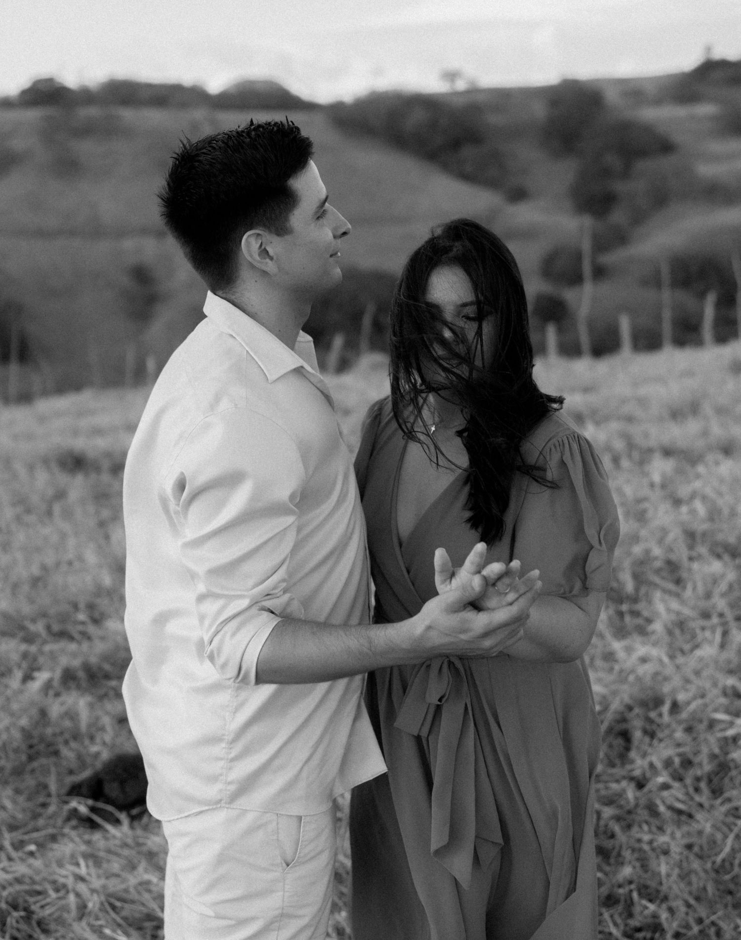 Black and white photo of a couple sharing an intimate moment in a meadow.
