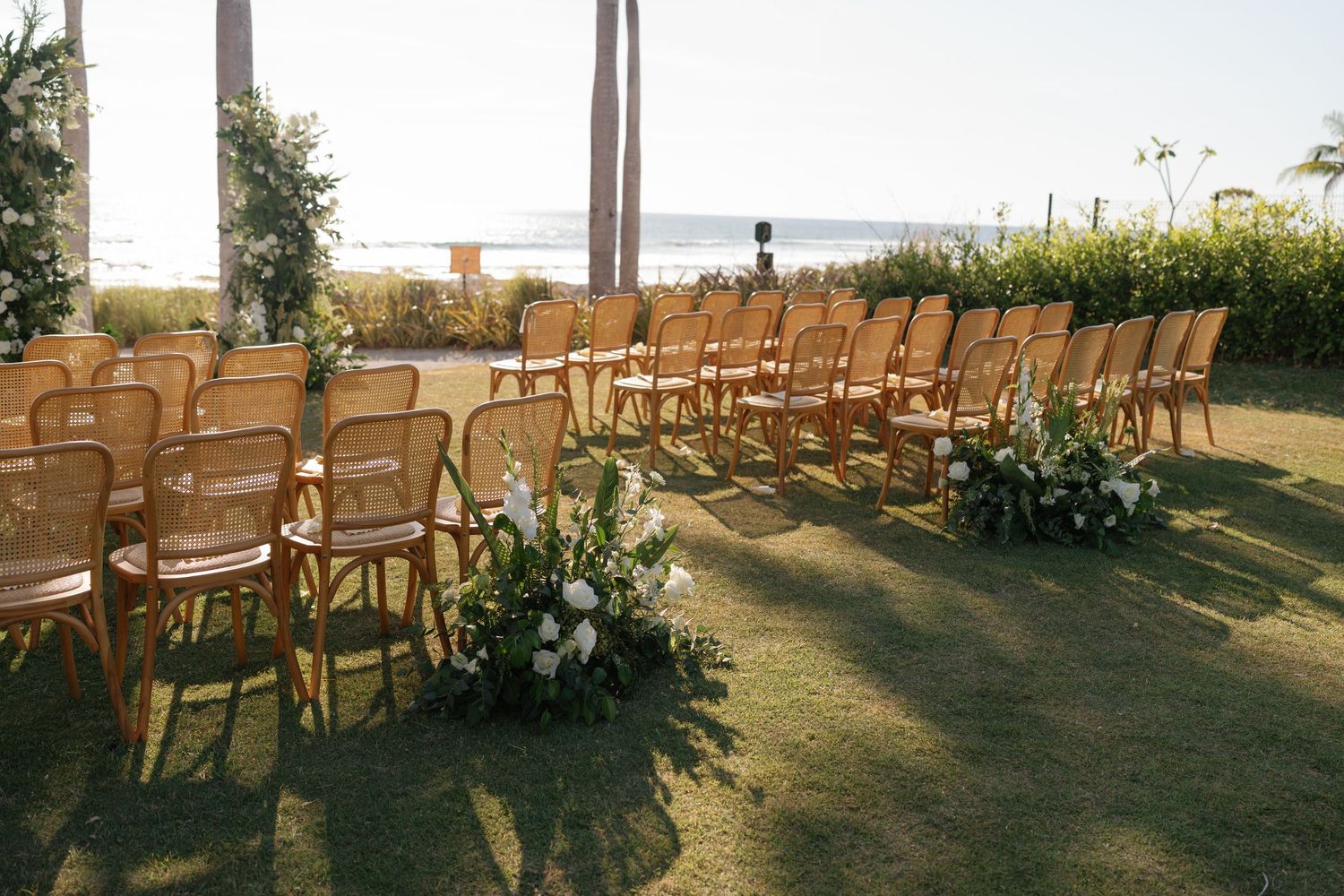 Wooden chairs set up for an outdoor wedding ceremony on a grassy lawn at sunset.