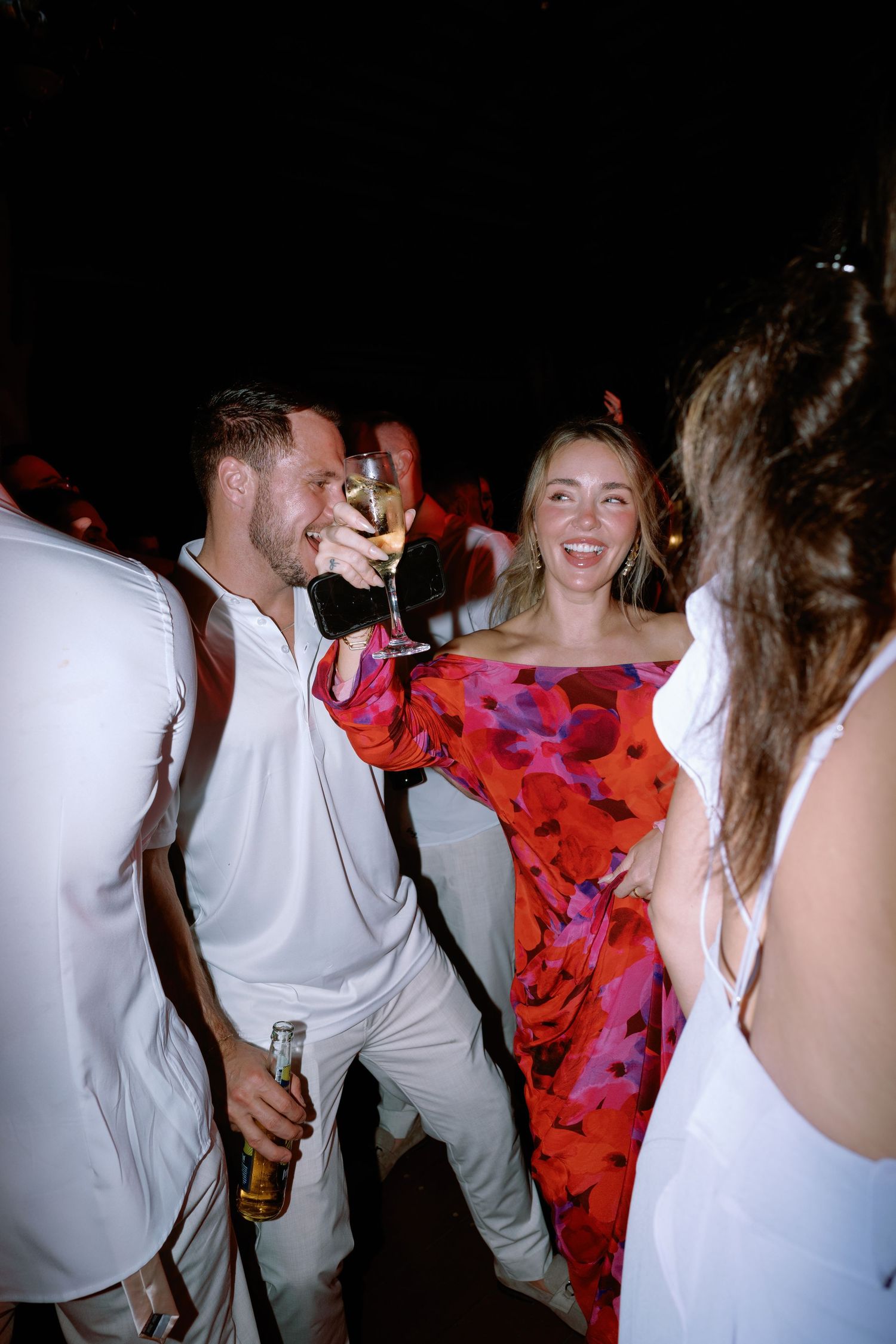 Wedding party dancing and celebrating at nighttime reception with vibrant decor.