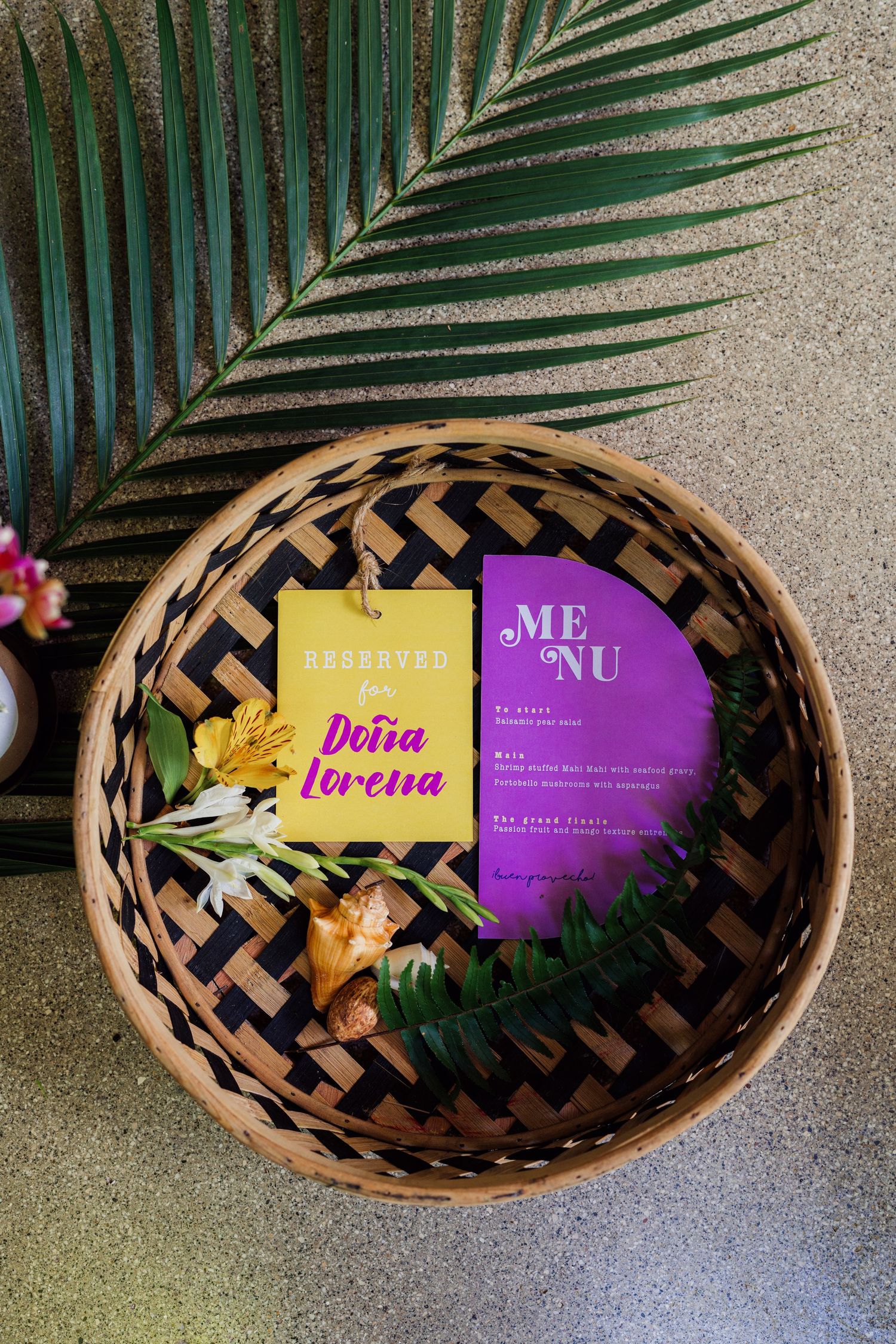 Decorative basket with palm fronds and colorful name cards for tropical themed wedding.