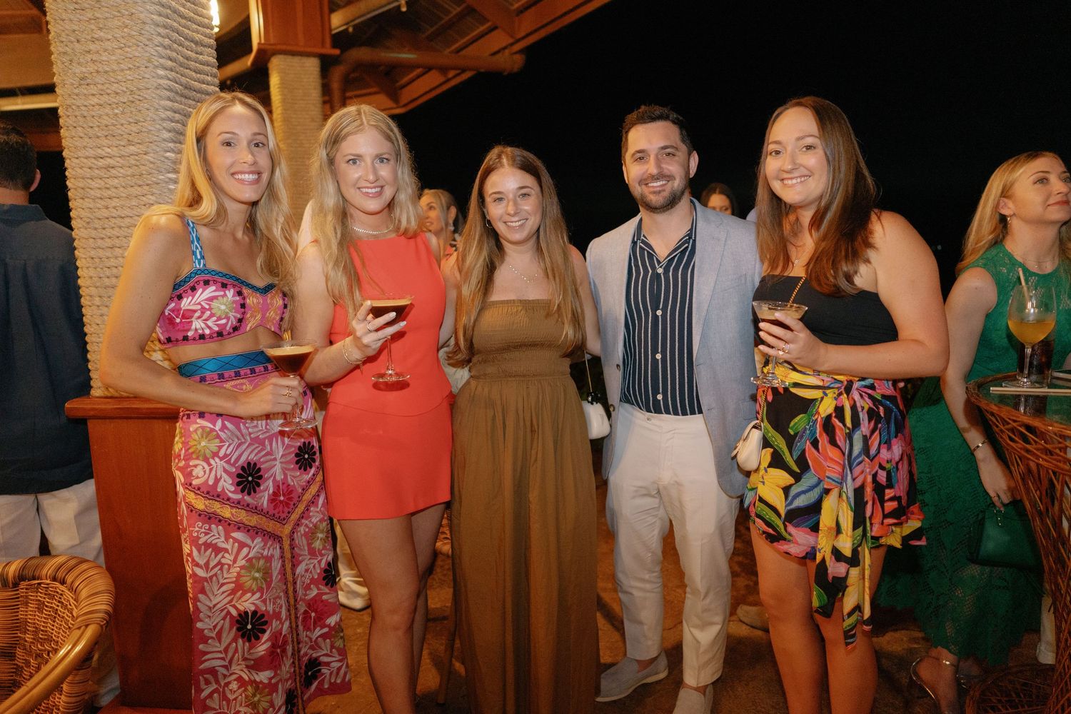 Group of friends in colorful attire gather for drinks at an evening social event.