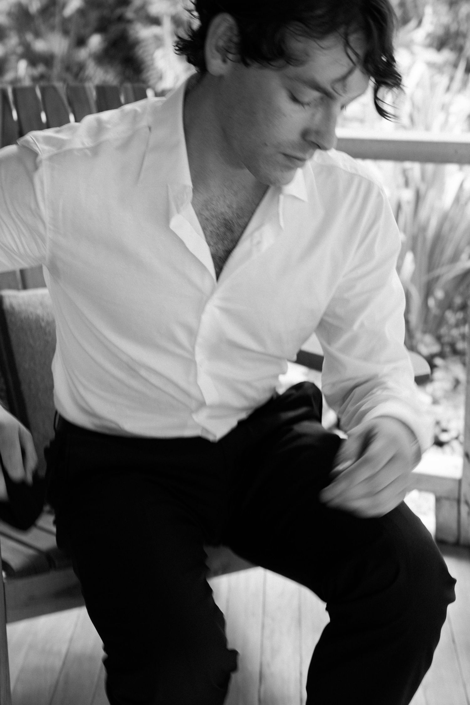 Man in white shirt sitting outdoors in casual pose on wooden chair.