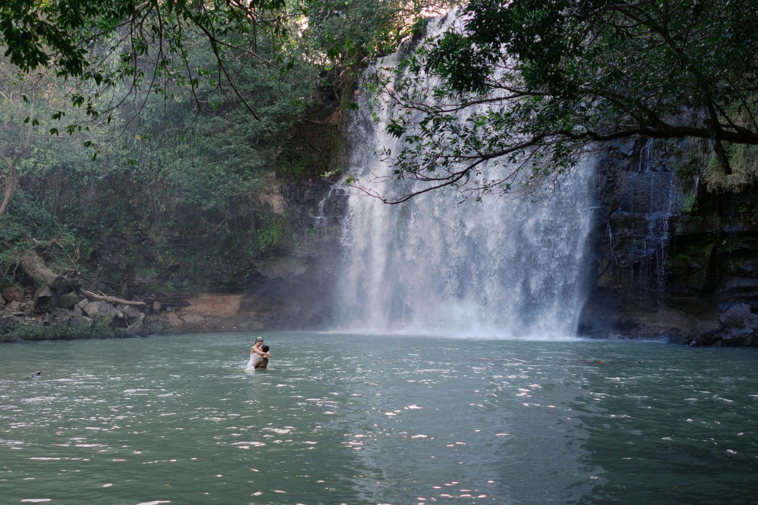 A distant view of a majestic waterfall with swimmers in the pool below.