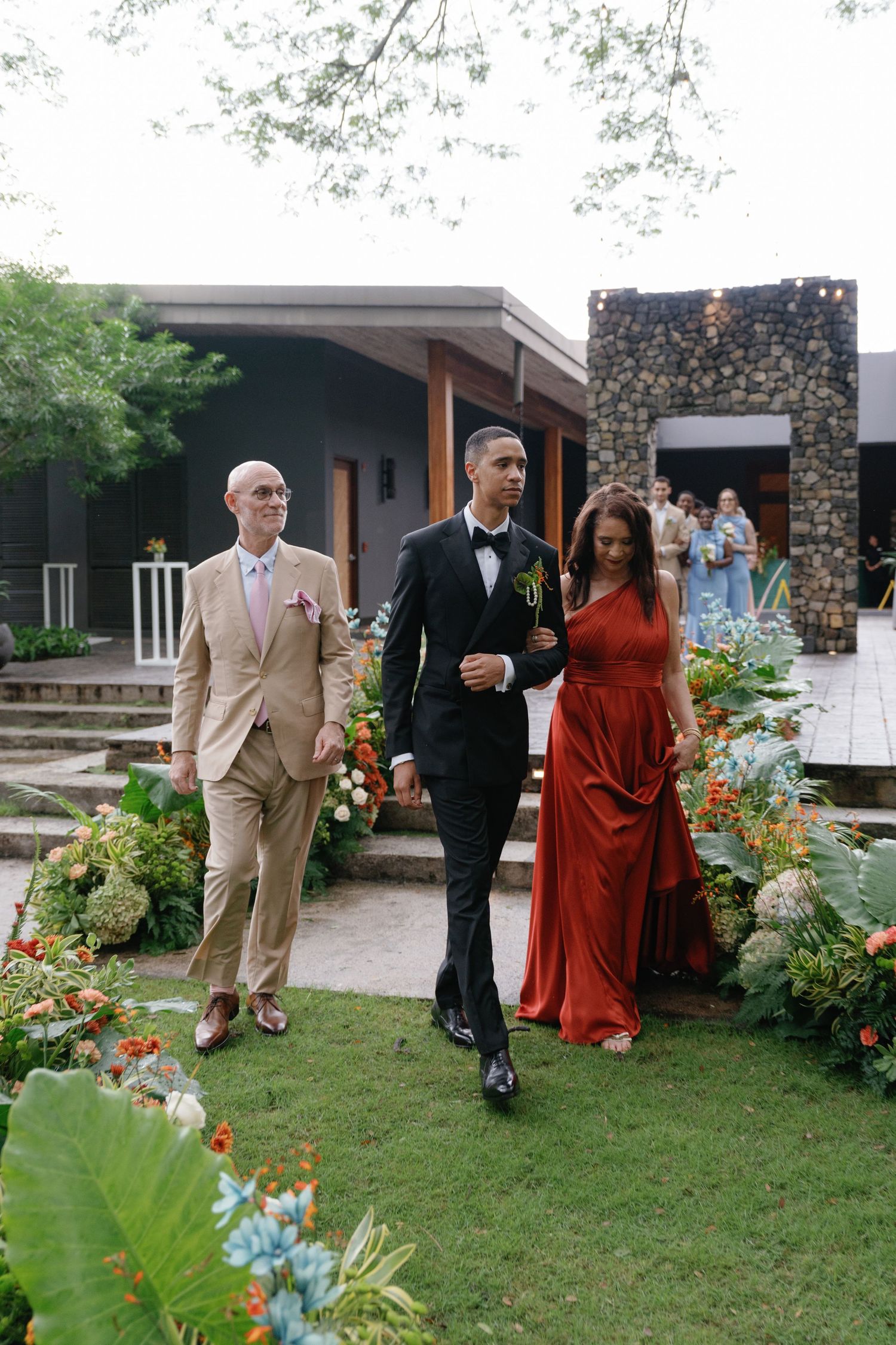 Wedding party walking through a garden path with colorful floral arrangements.