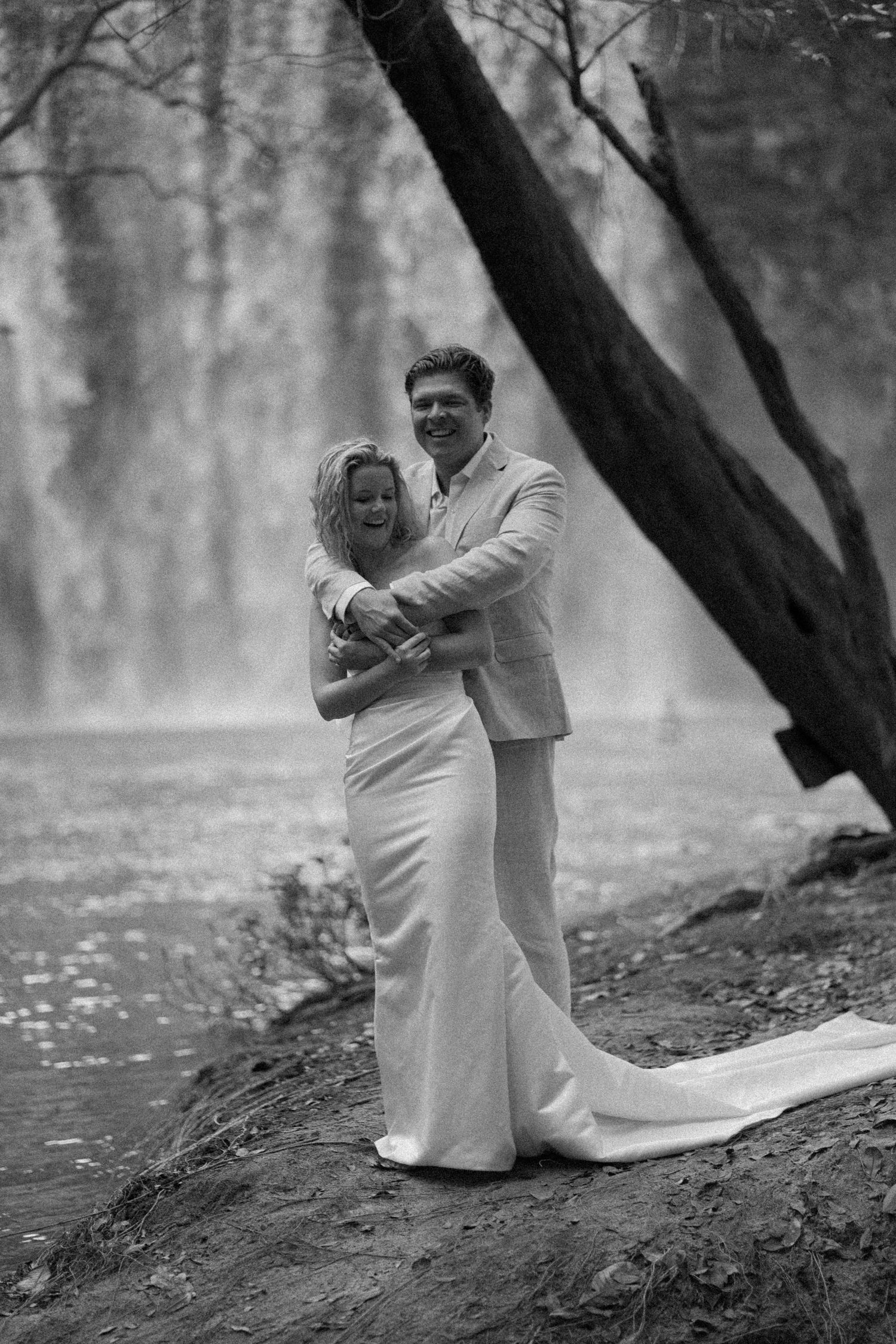 Black and white wedding portrait by misty waterfall with dramatic lighting.