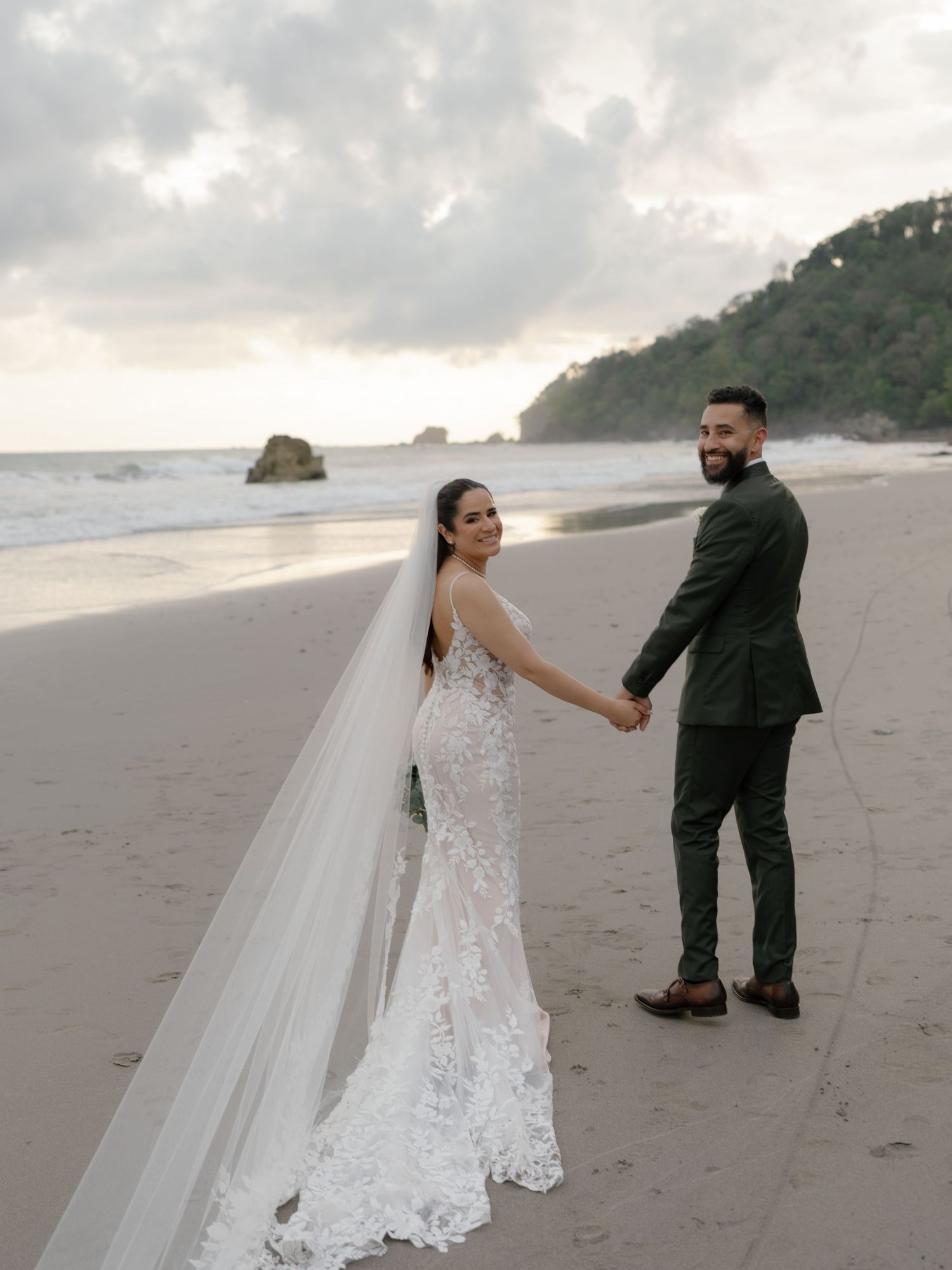 Newlyweds walk hand in hand along a scenic beach at sunset.