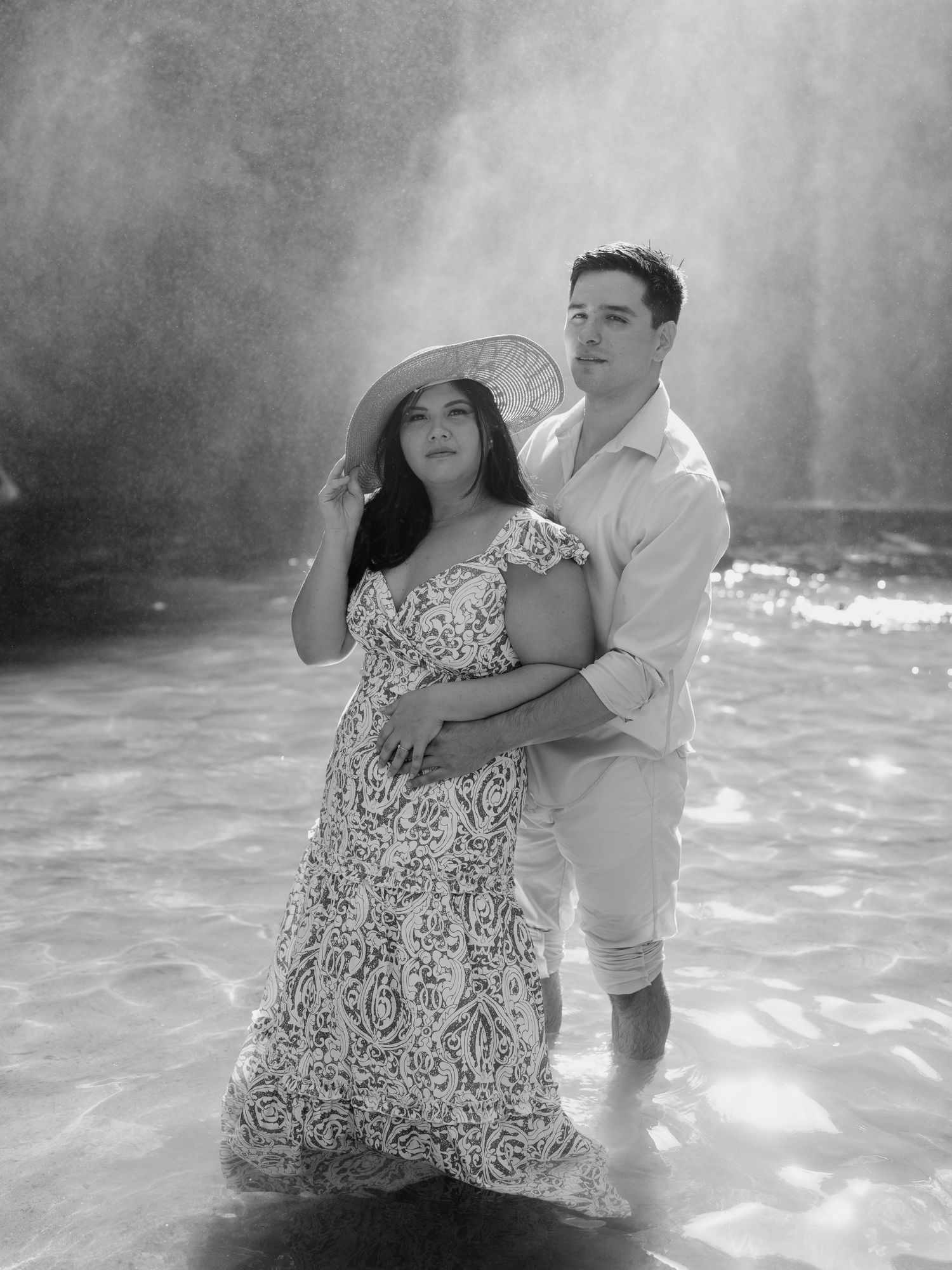 Black and white photo of a couple dancing playfully in shallow water with ethereal mist surrounding them.