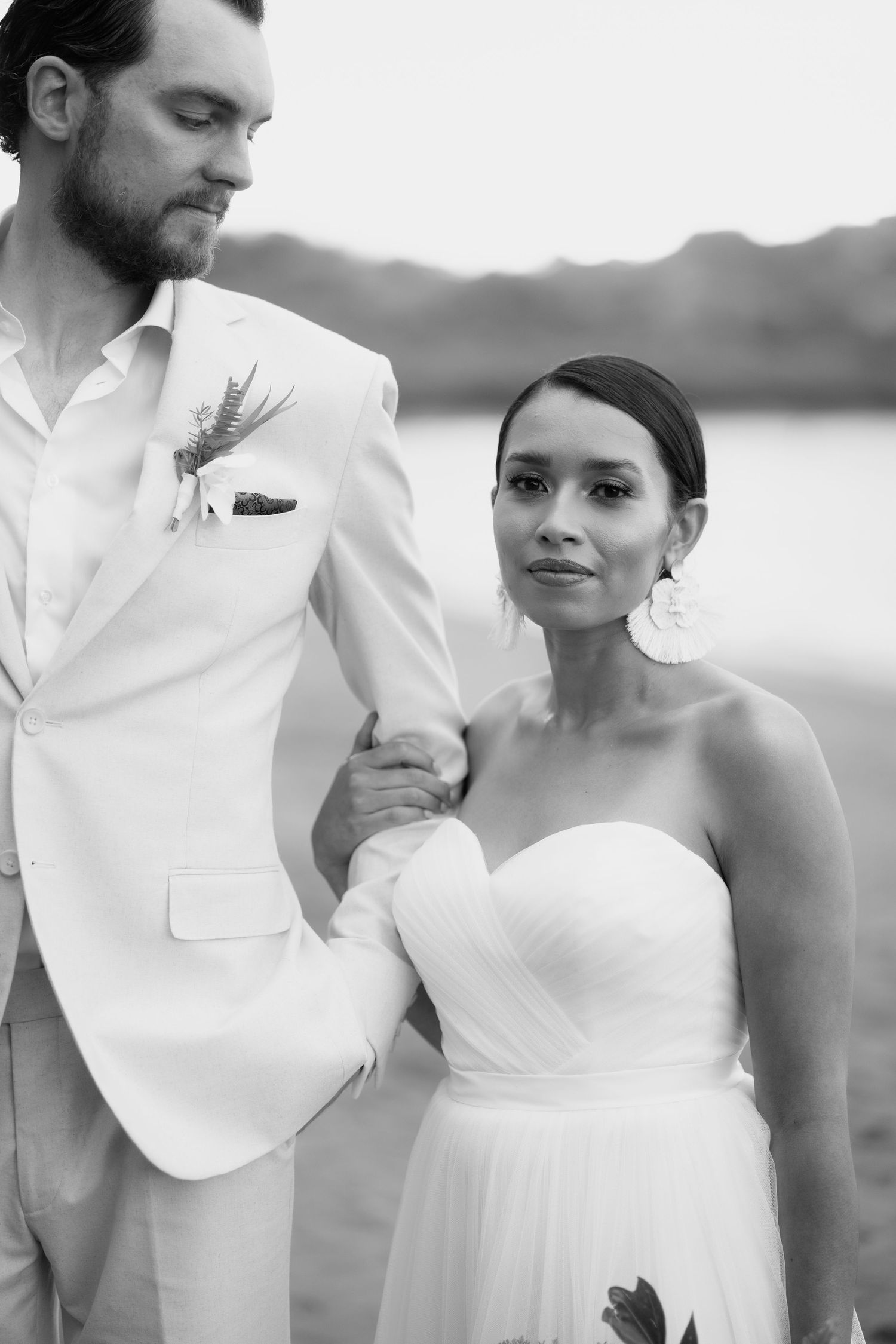 Elegant black and white wedding photos capturing tender moments between a couple by the water.