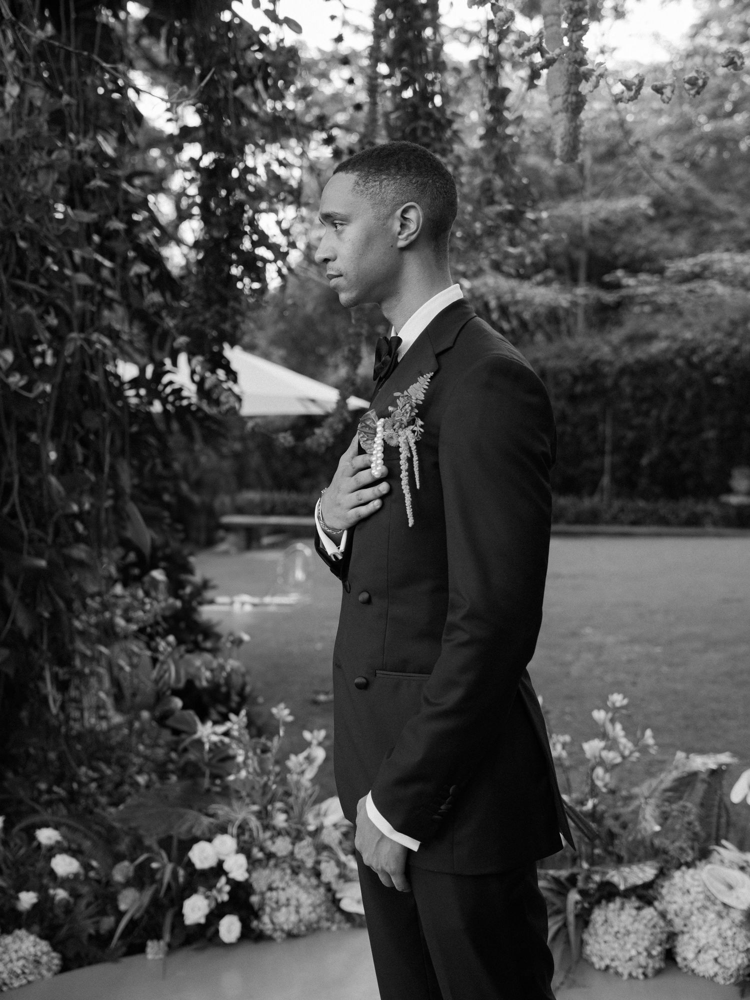 Black and white photo of wedding party members posing by floral arrangements outdoors.