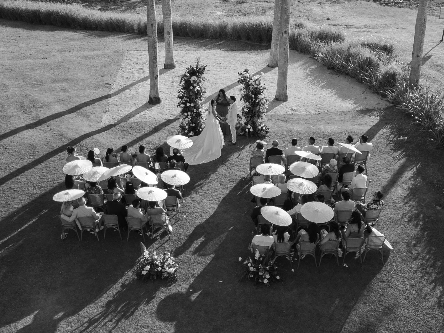 Aerial black and white view of outdoor wedding reception with round tables under string lights.