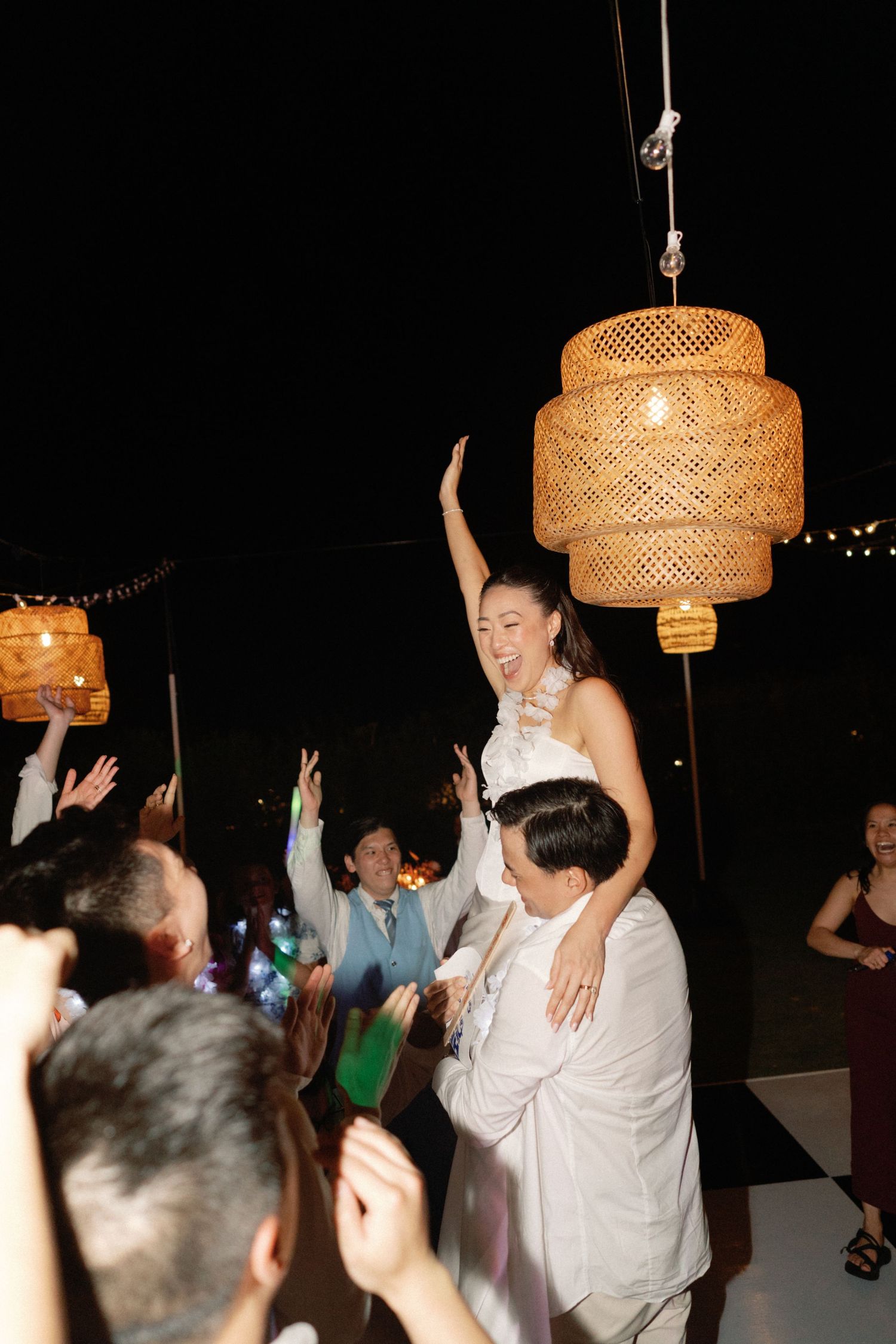Wedding celebration with guests dancing under woven pendant lights at night.
