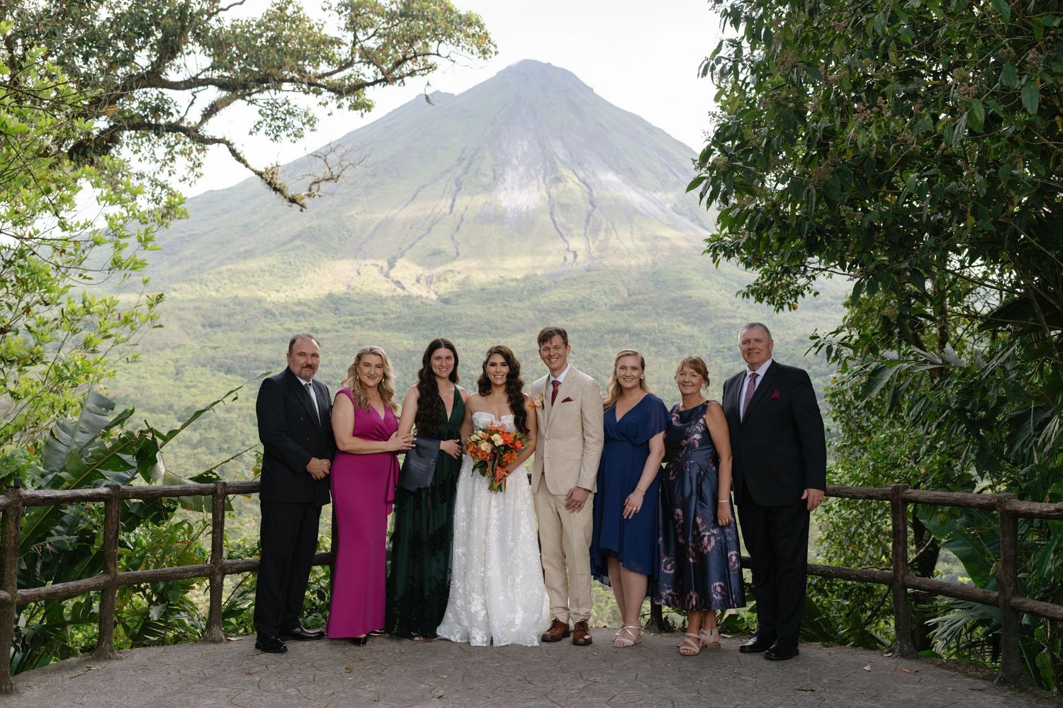 Wedding party poses for group photos on scenic mountain overlook with rustic railing.