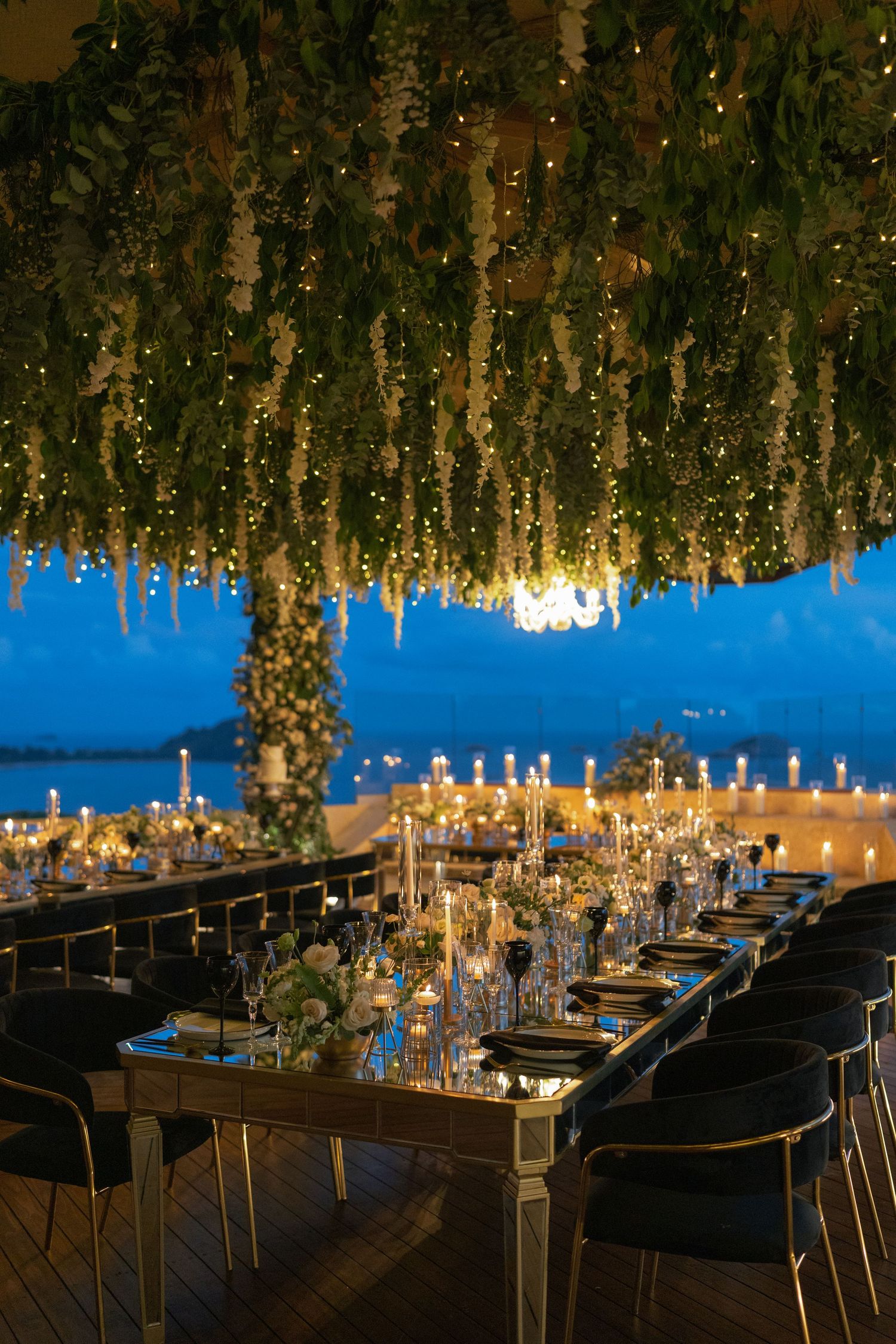 Romantic wedding reception table setting with hanging greenery and warm lighting.