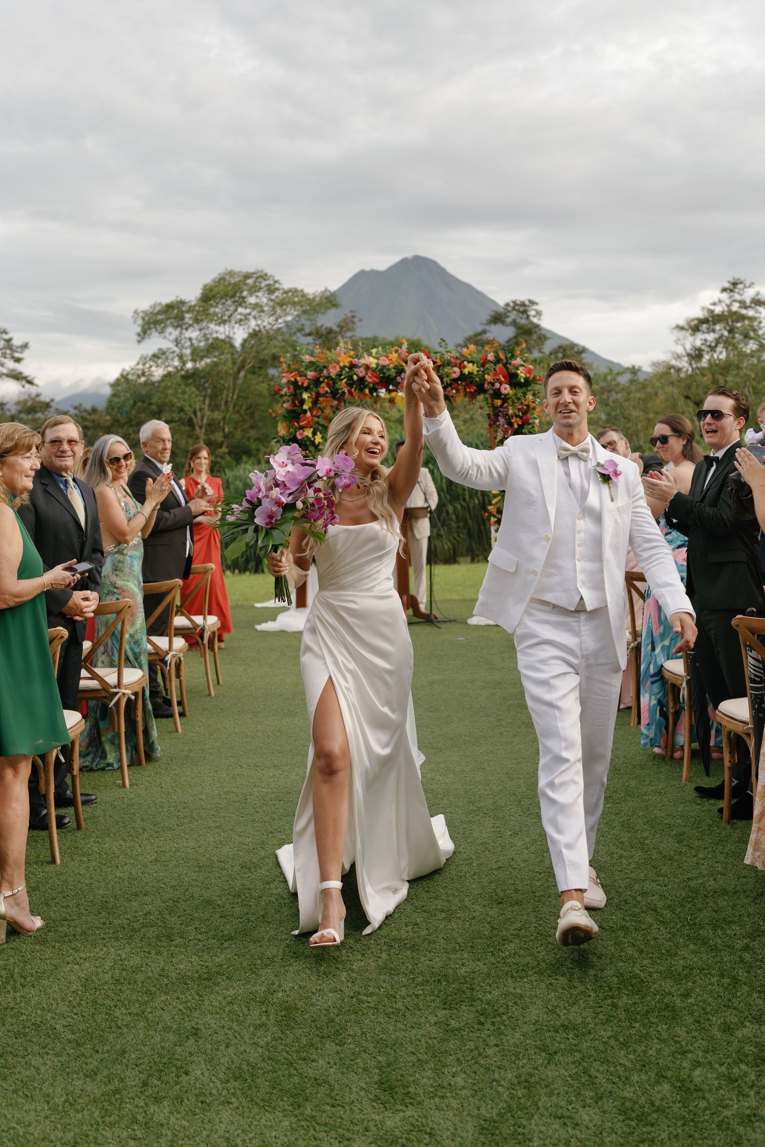 Wedding party walking down the aisle on grass with a mountain backdrop.