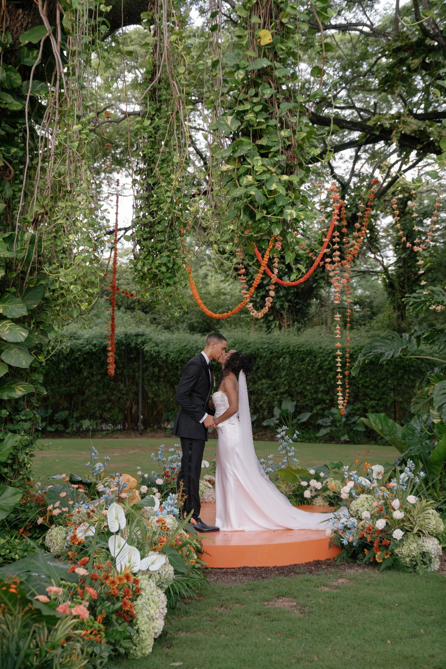 Garden wedding ceremony setup with orange string lights and floral arrangements on a circular platform.