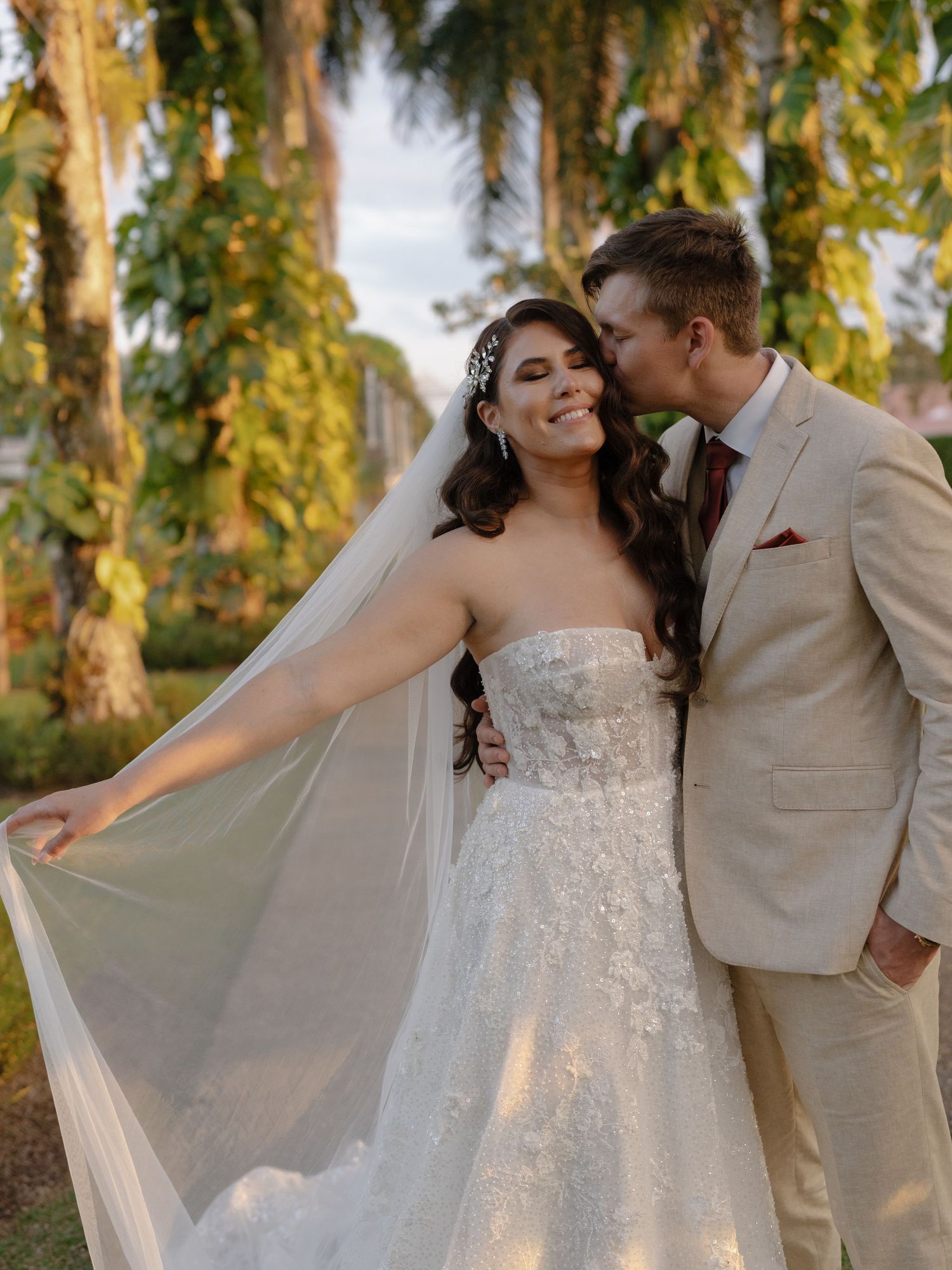Newlyweds share playful moments under palm trees in a tropical garden setting.