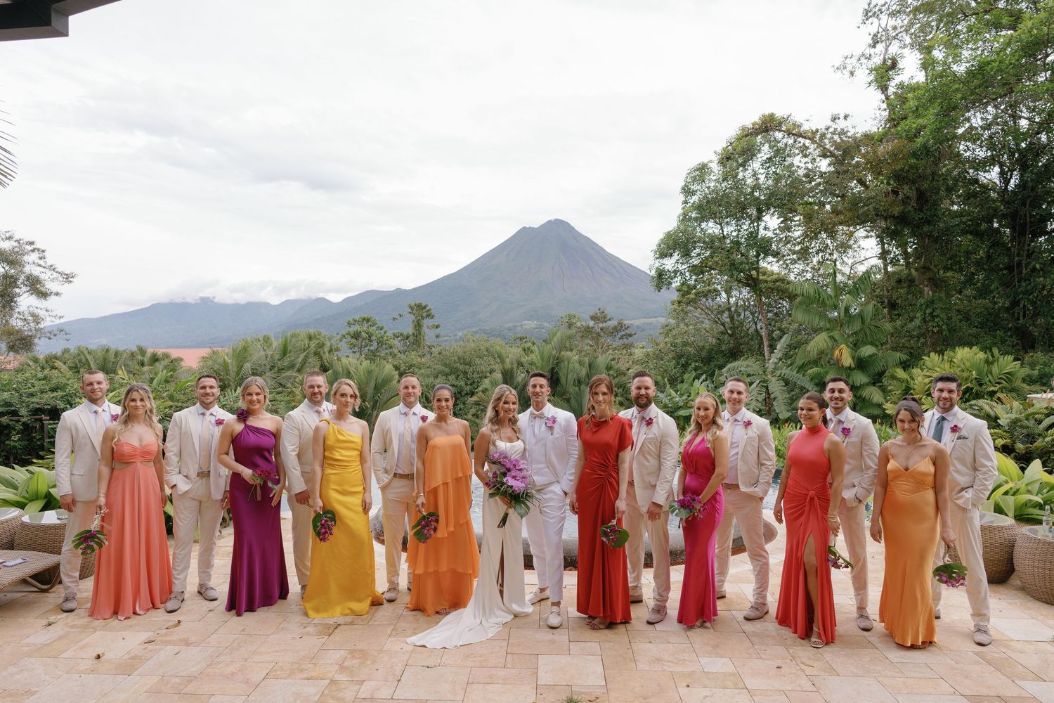 Wedding party in coral and orange dresses posed with mountain backdrop.