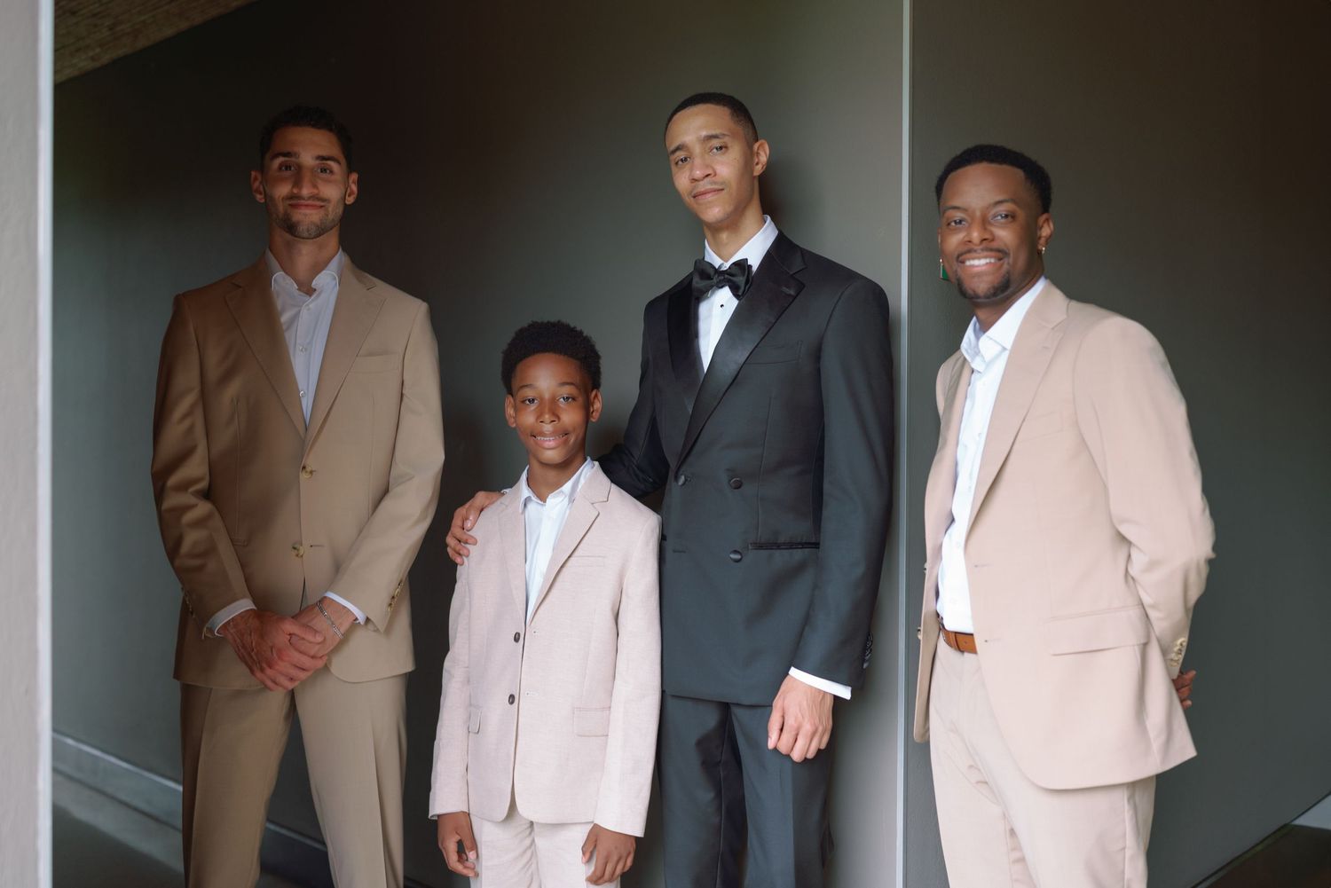 Formal group photo of wedding party members in light-colored suits.