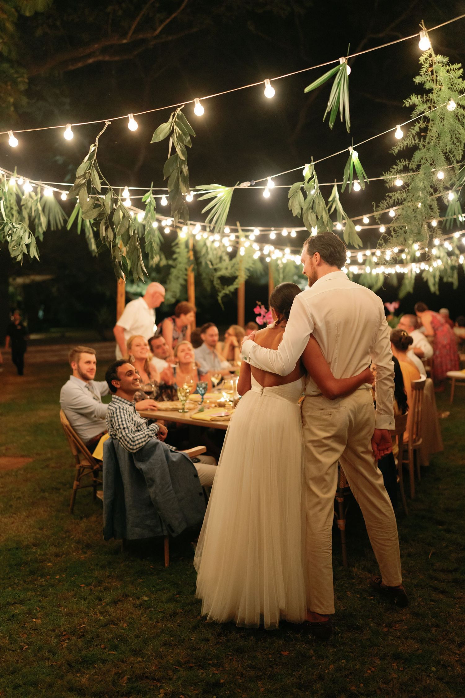 Guests enjoy an outdoor evening reception under string lights at a garden wedding celebration.