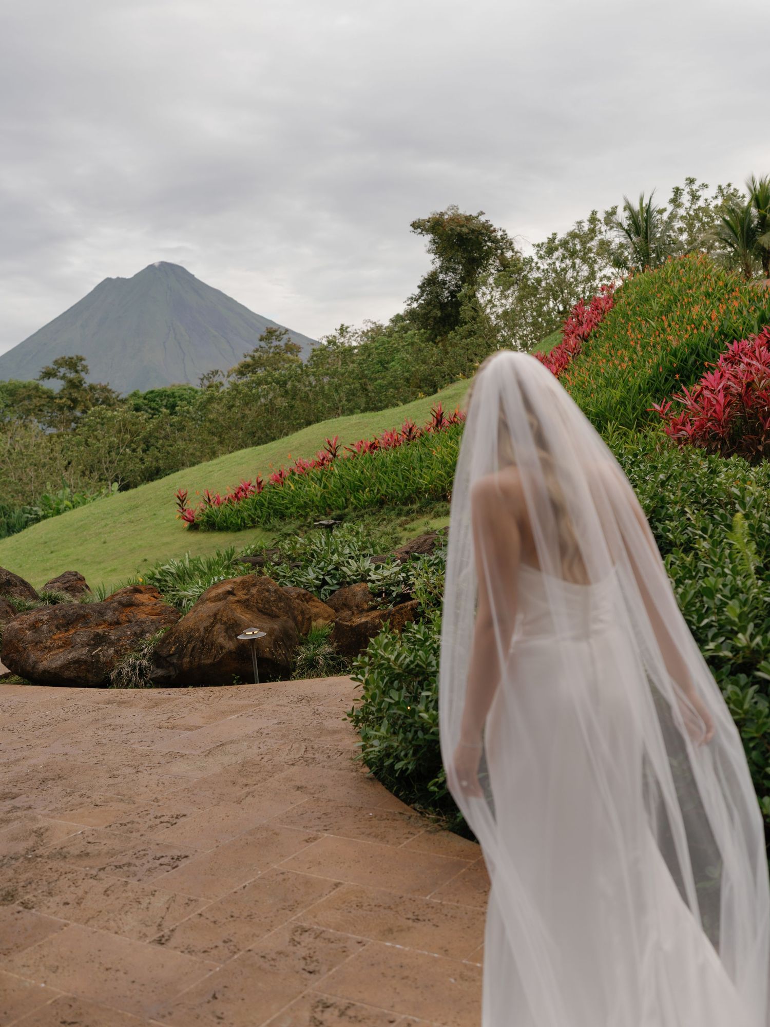 Wedding veil flows in the foreground of a dramatic mountain landscape with red flowers.