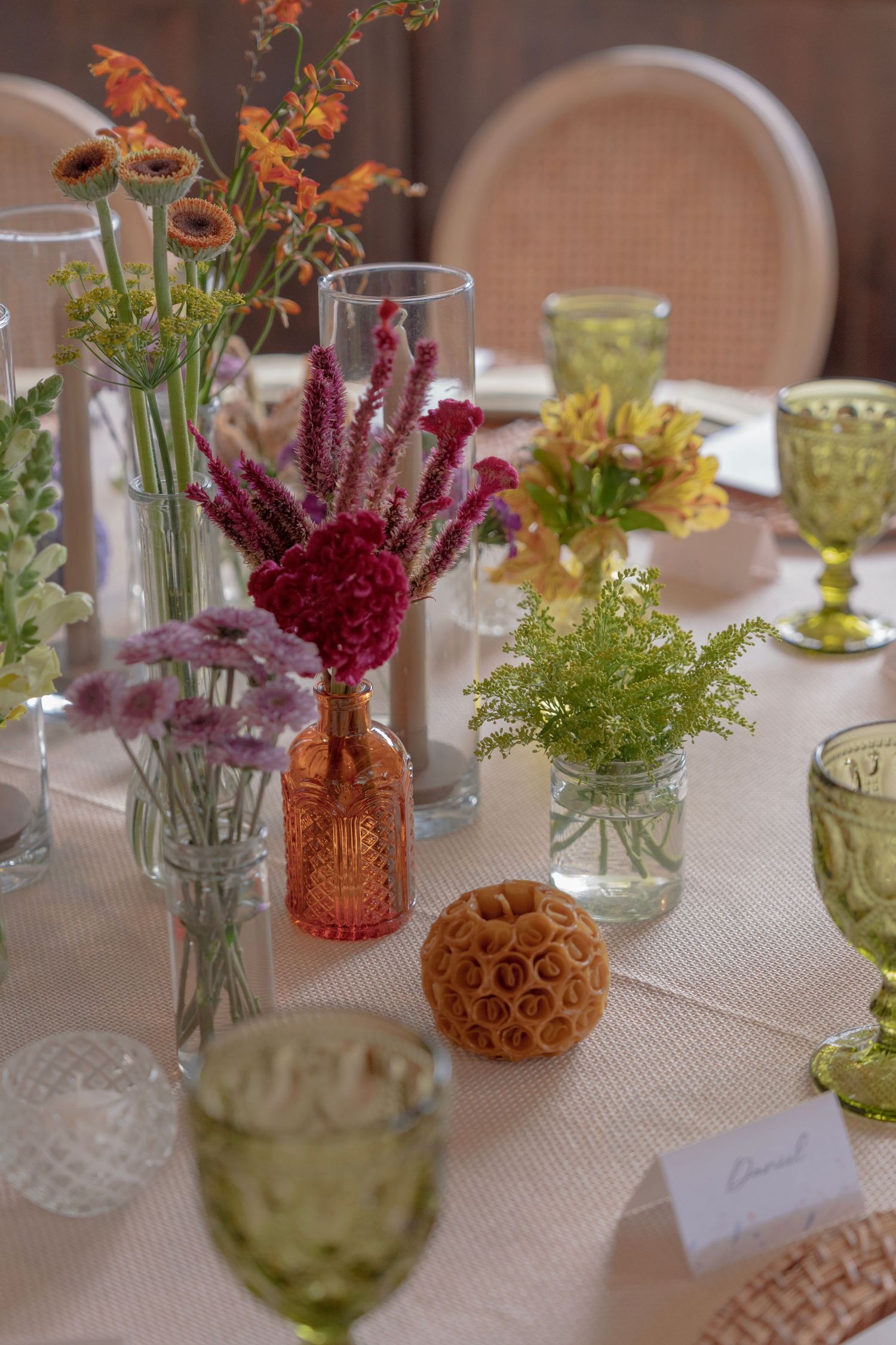 Elegant table settings with small glass vases holding colorful wildflowers and vintage-style colored glassware.