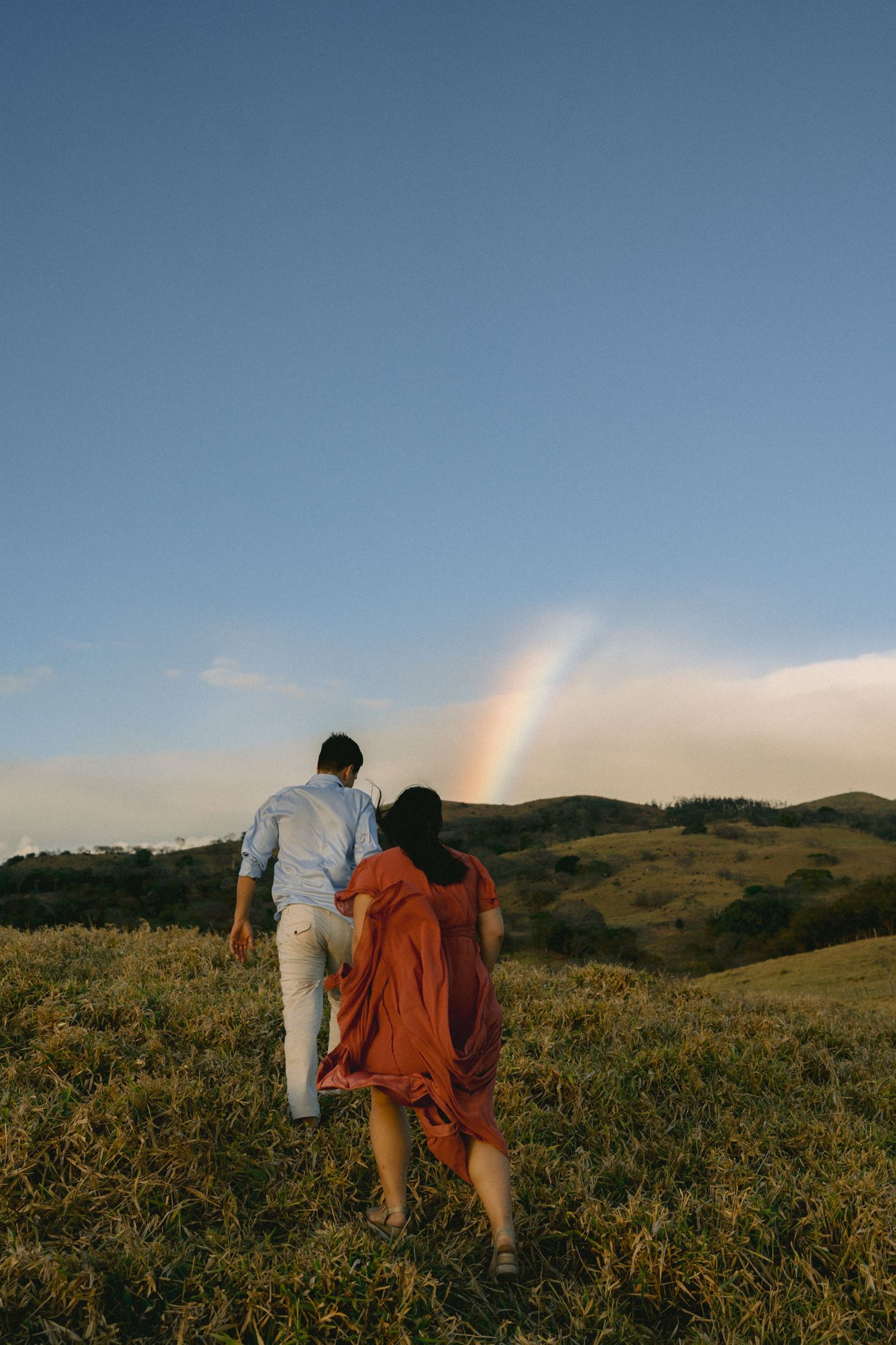 Two people walk through a scenic hilltop meadow during golden hour.