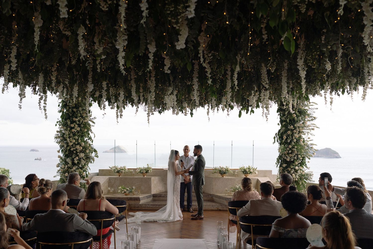 Wedding ceremony setup with hanging greenery and ocean view.