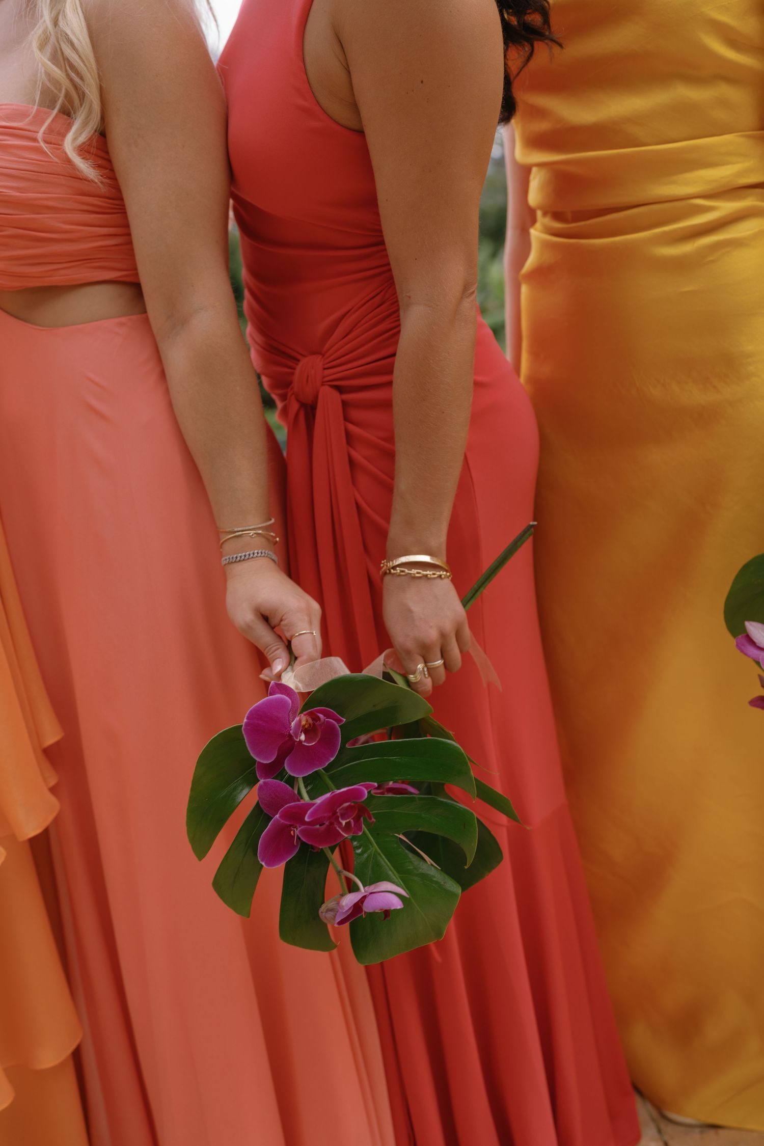 Close-up of bridesmaids holding purple orchid bouquets in warm-toned dresses.