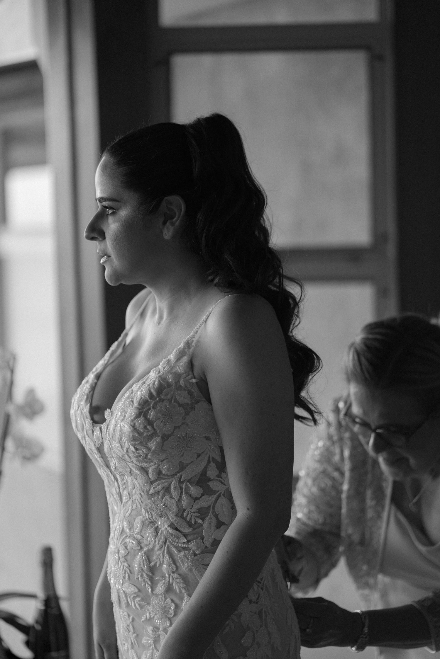 Wedding dress preparation moment captured in dramatic black and white photography.