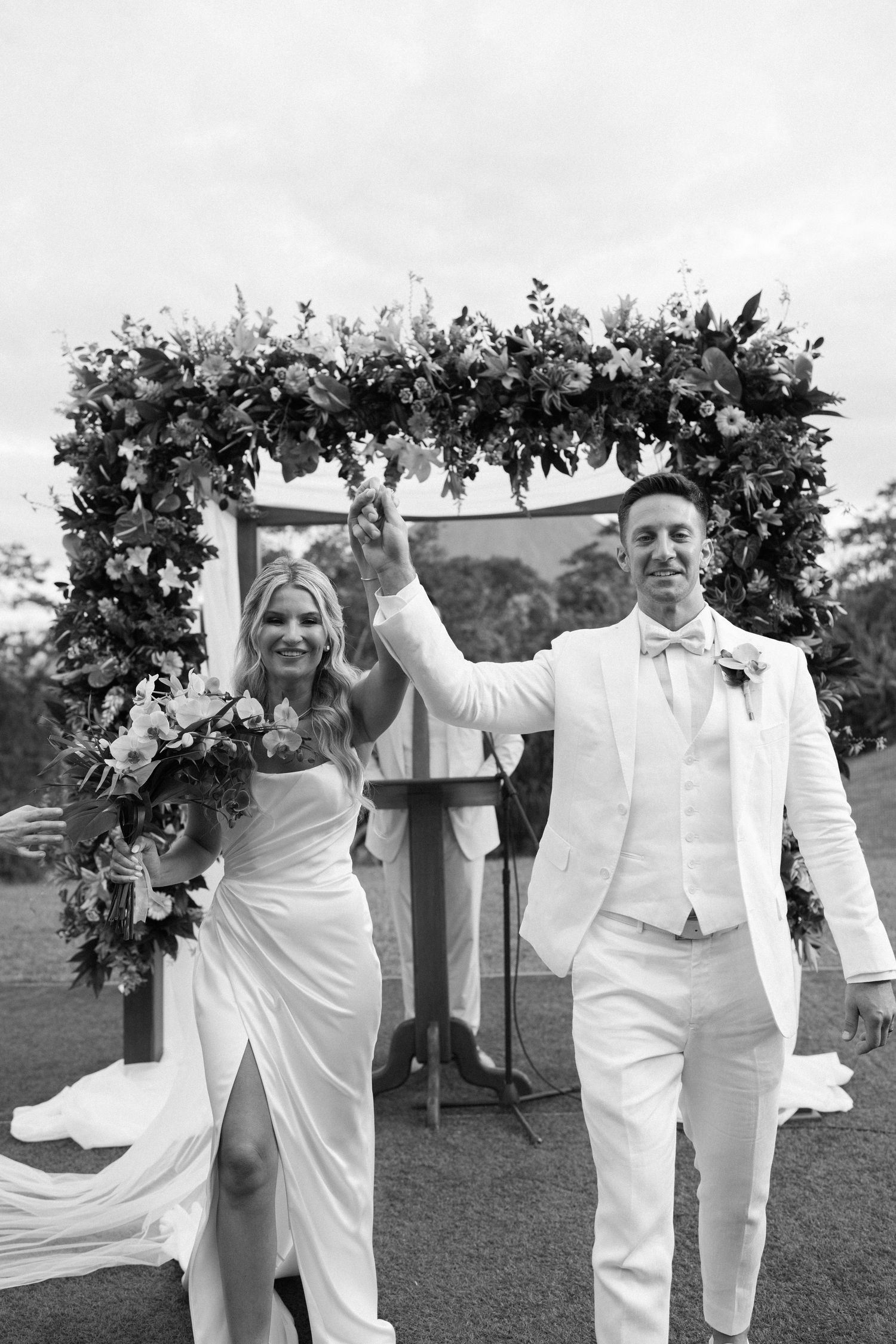 A wedding couple celebrates under a floral arch during their outdoor ceremony.