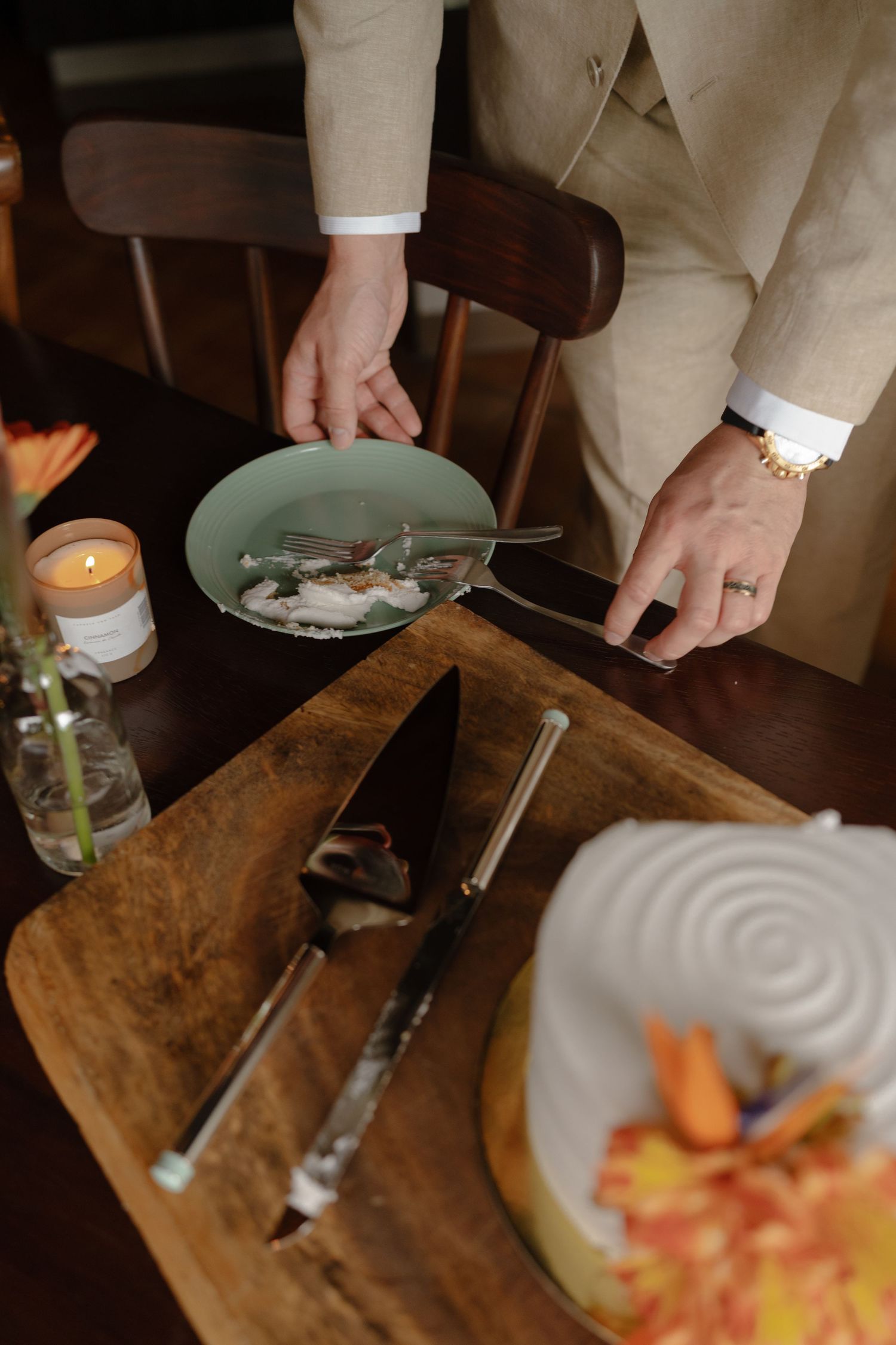 Close-up of hands cutting into a white wedding cake on a rustic wooden surface.
