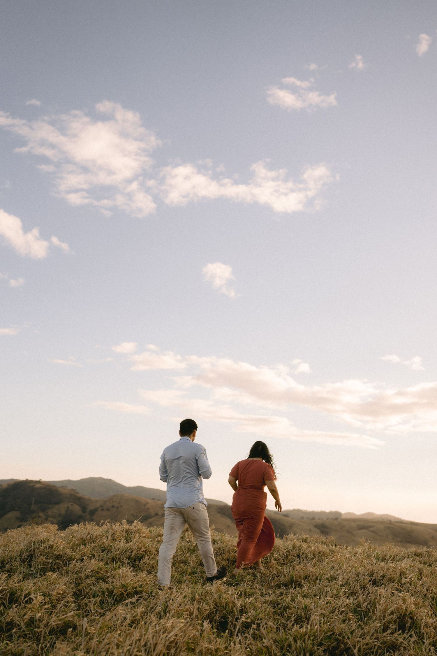 Silhouettes of two people walking together across a scenic hilltop at dusk.