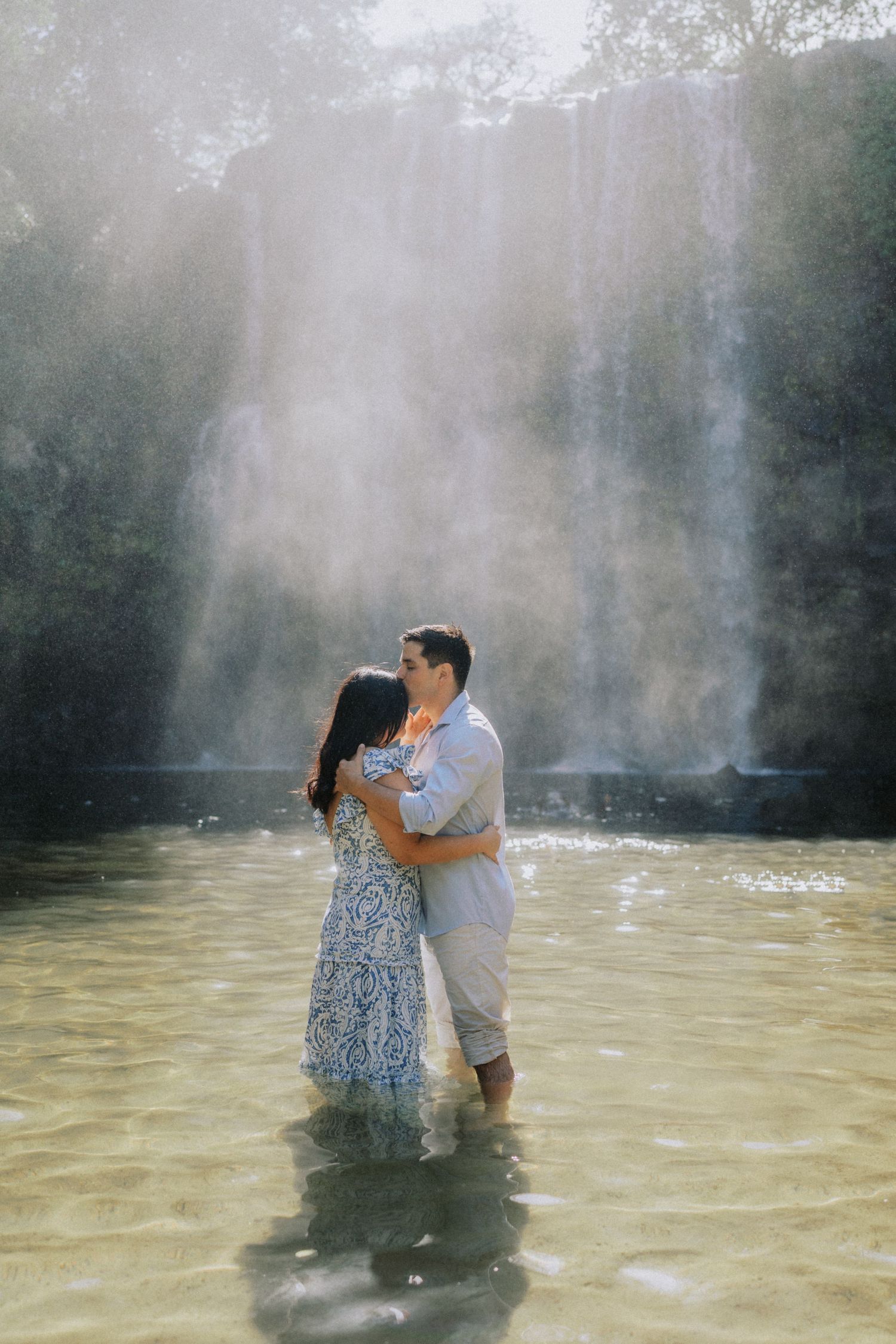 Couple embraces in misty water during an intimate photoshoot with dramatic lighting.