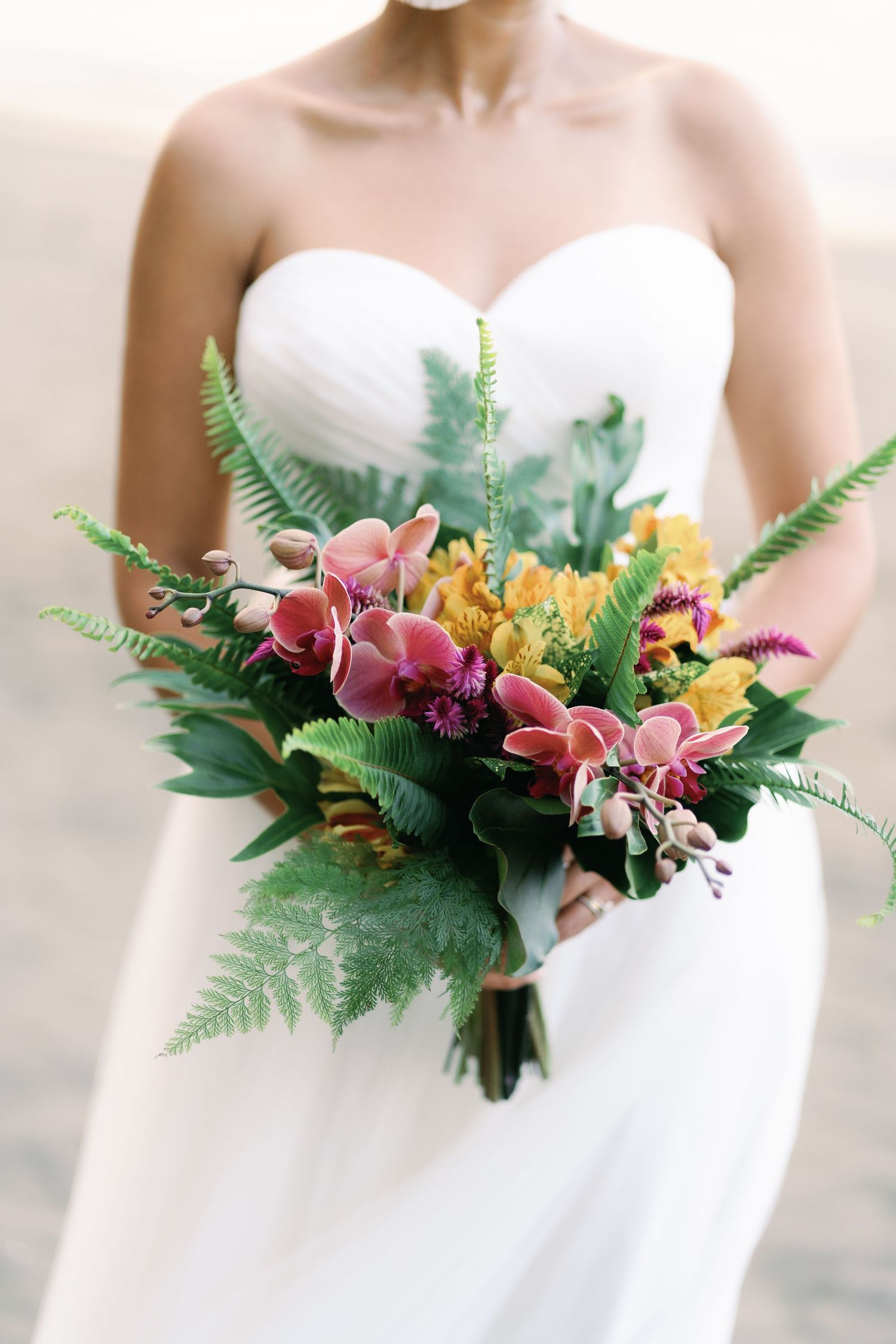 Close-up shots of a tropical wedding bouquet with pink orchids, yellow flowers and ferns.
