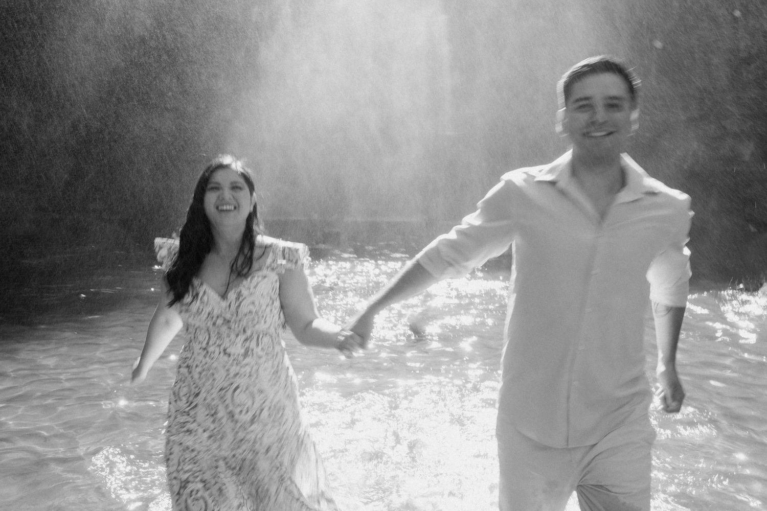 Black and white photo captures playful moments of a couple in misty water.