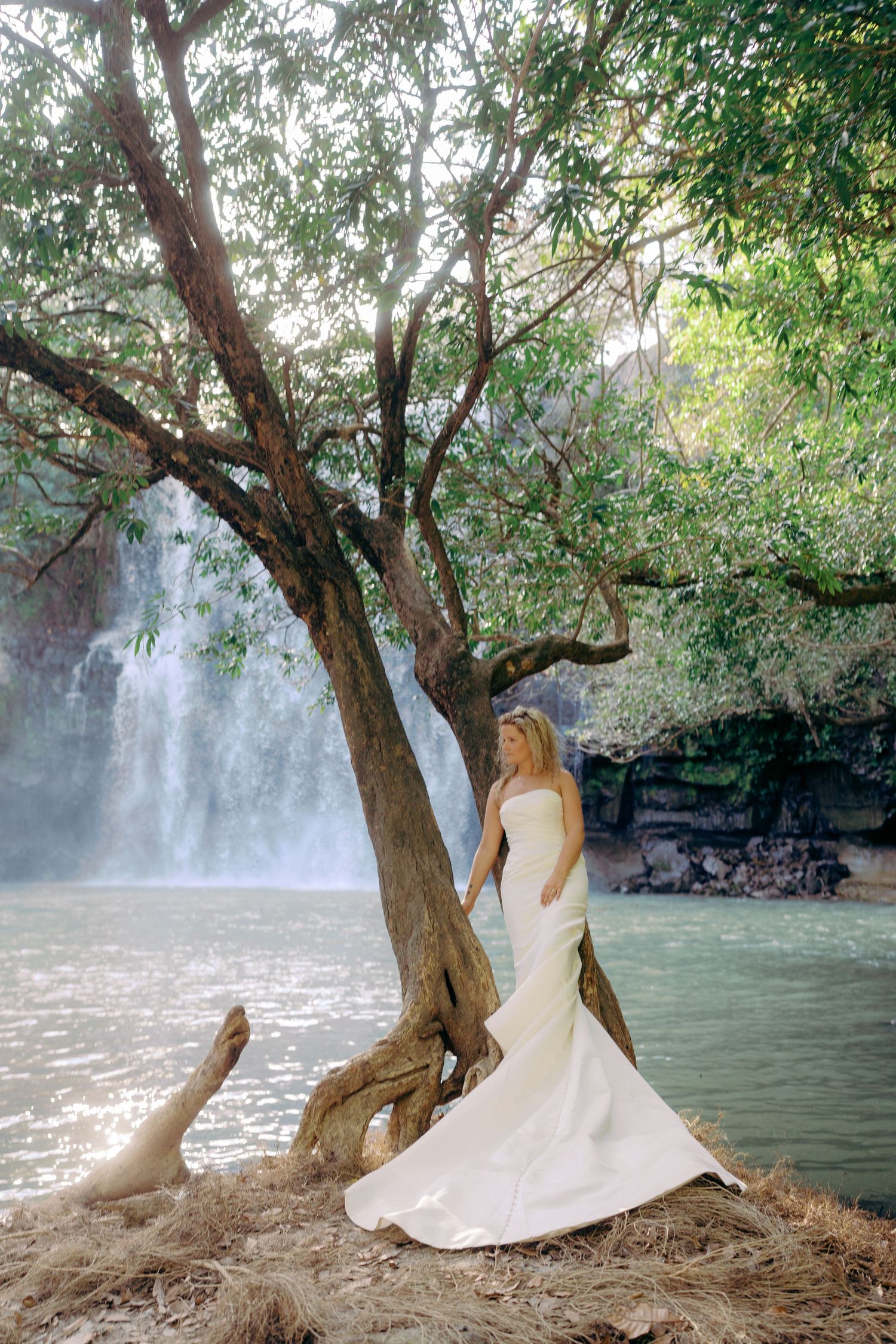 Wedding photos by a waterfall with flowing white dress against natural scenery.