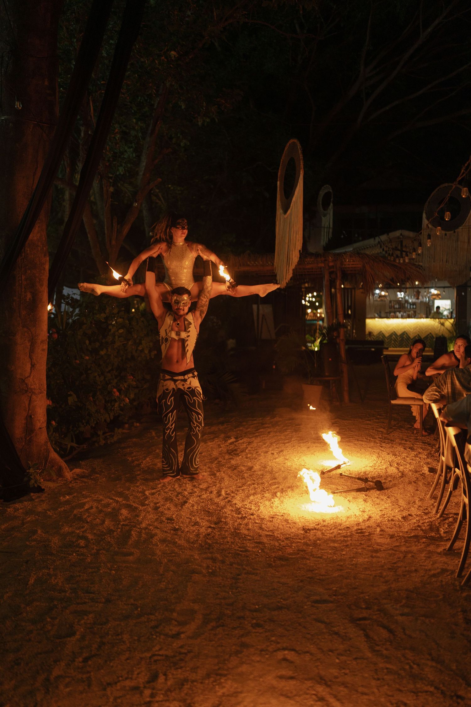 Fire dancers performing on a dark beach with flaming batons creating dramatic light trails.