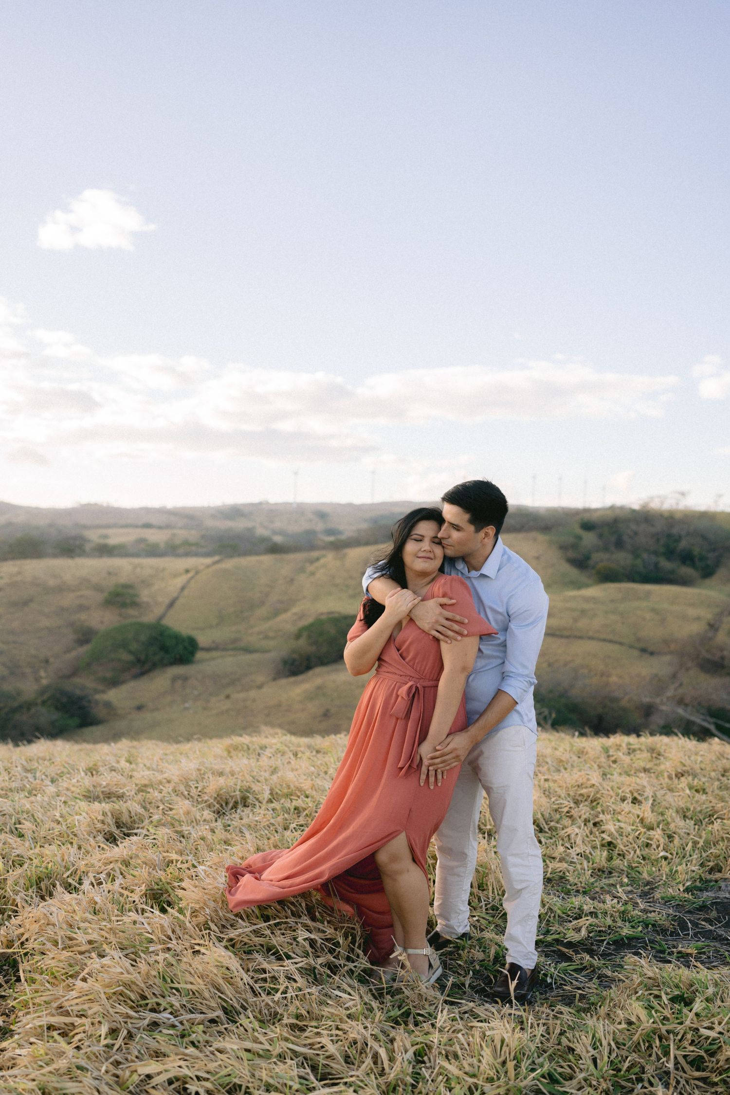 A couple dances together on a scenic hillside during a golden sunset photoshoot.