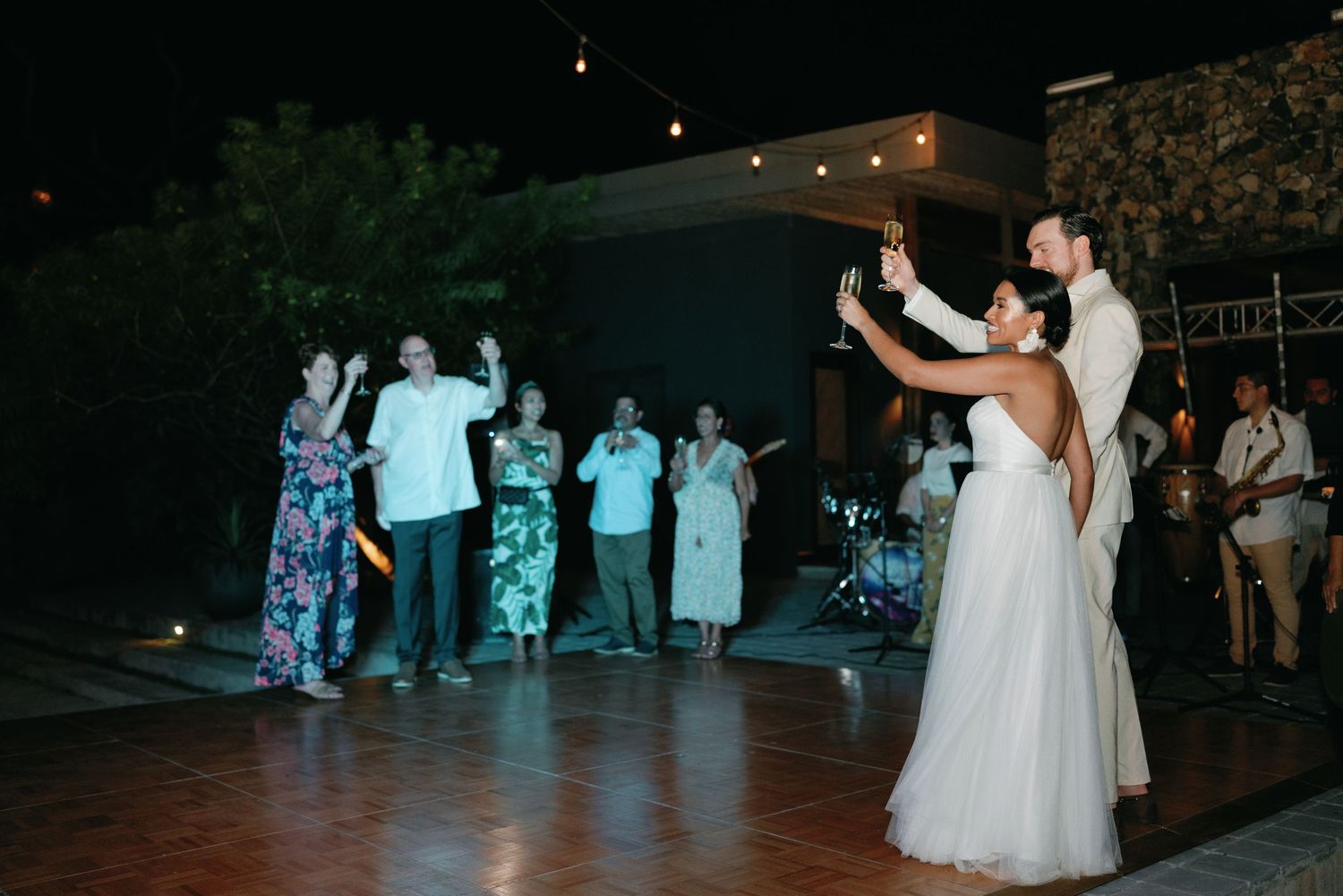 Wedding reception dance floor illuminated by string lights in an outdoor evening setting.