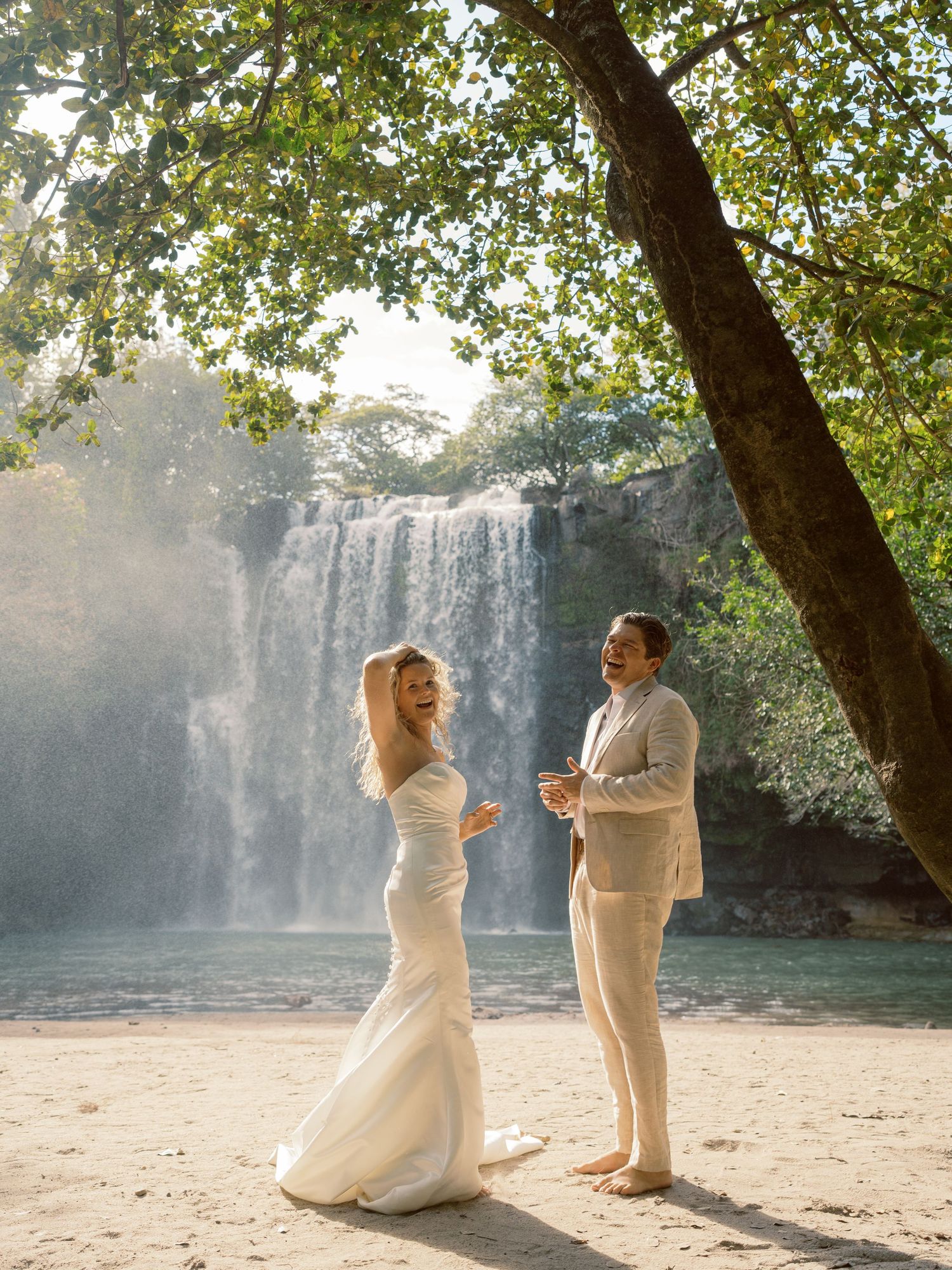 Couple in light-colored formal wear dancing by a waterfall.