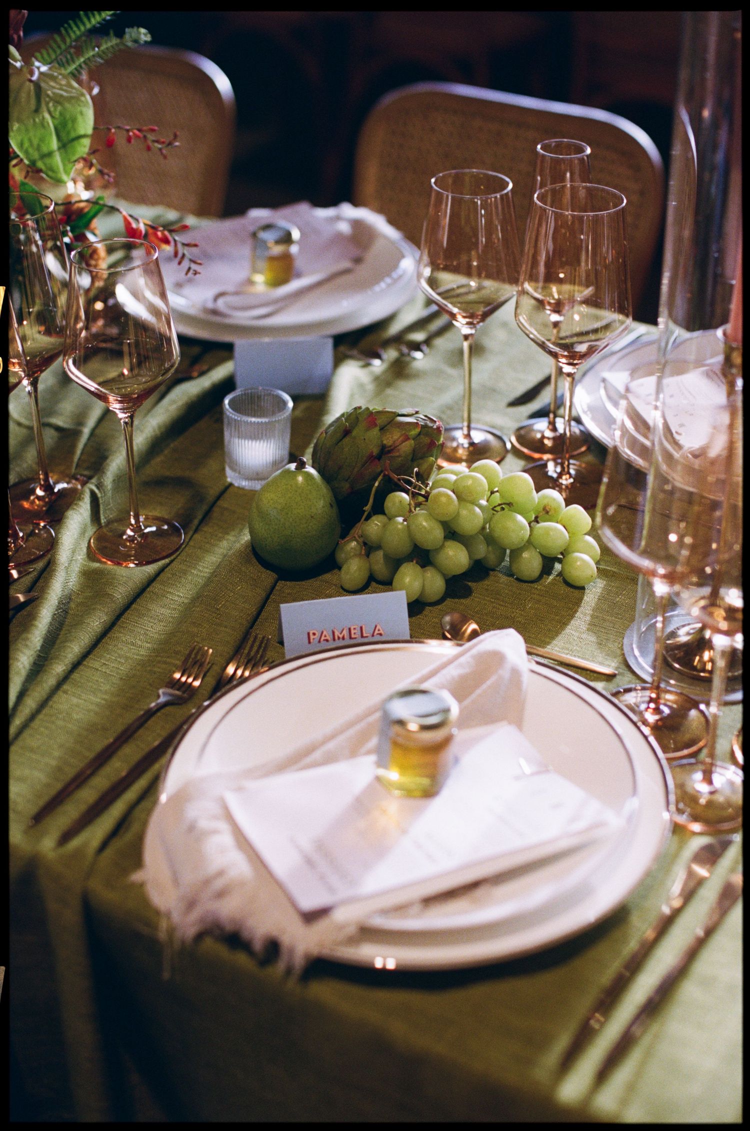 Elegant table settings with white plates, wine glasses, and fresh green grapes on a sage green tablecloth.