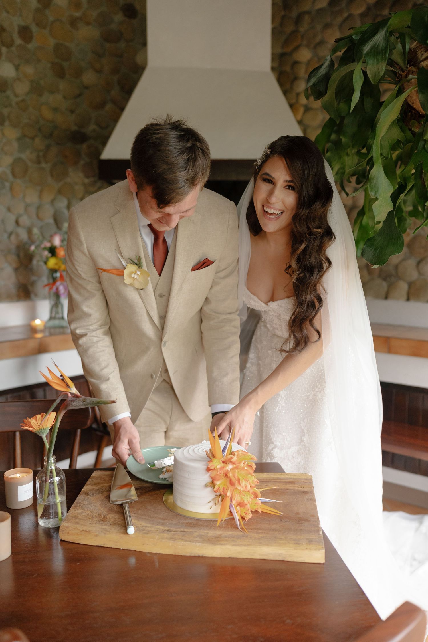 Couple cutting their wedding cake together on a wooden table with floral decorations.